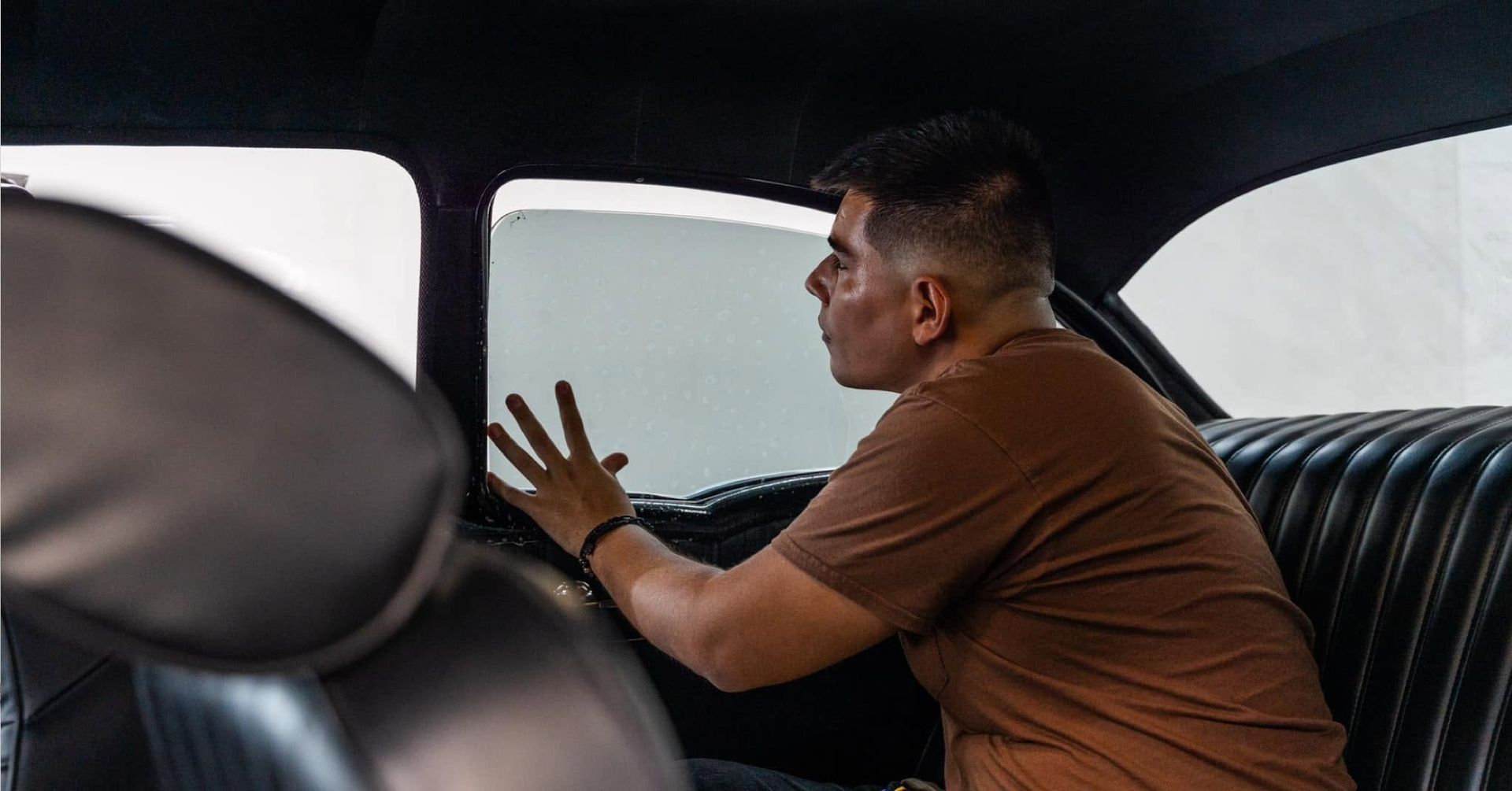 Man sitting in a car, looking out the window with hands raised toward the glass.
