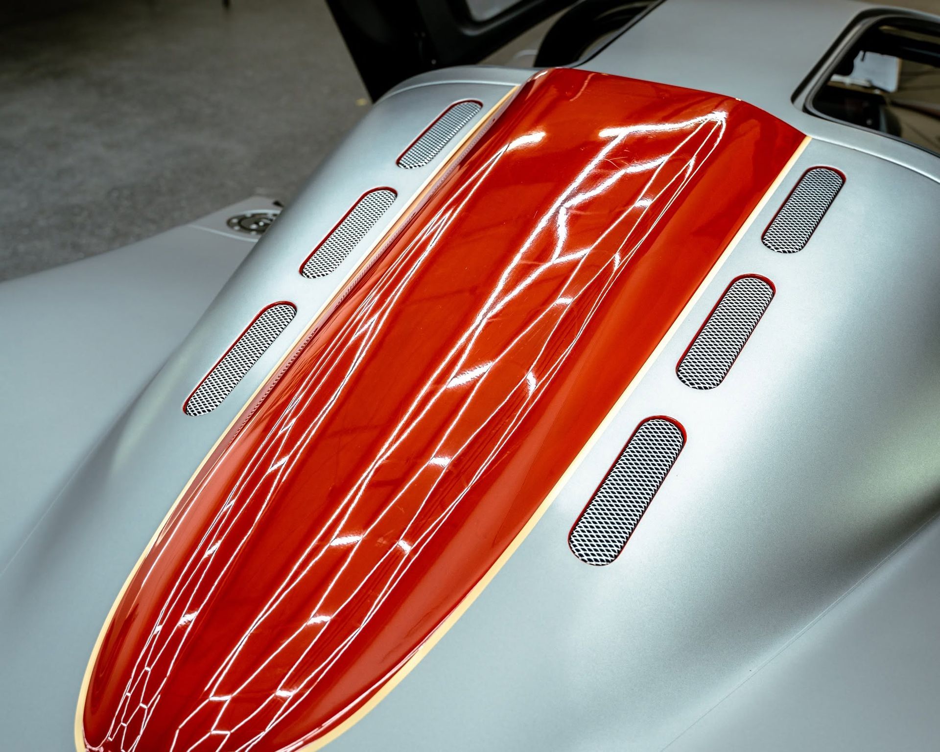 Close-up of a white race car hood with a bright red central stripe and silver vent grilles