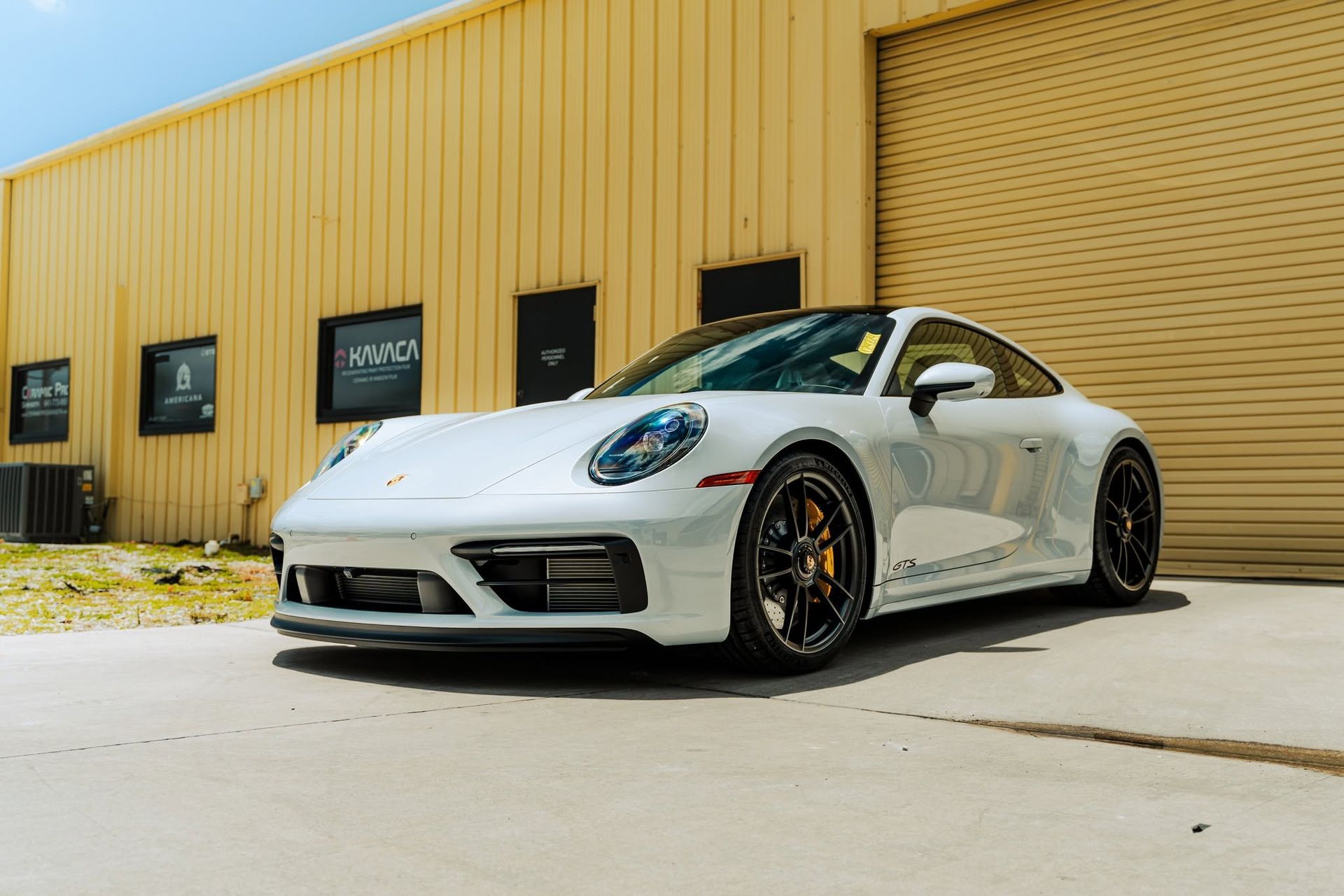 White Porsche 911 parked beside a yellow industrial building on a sunny day