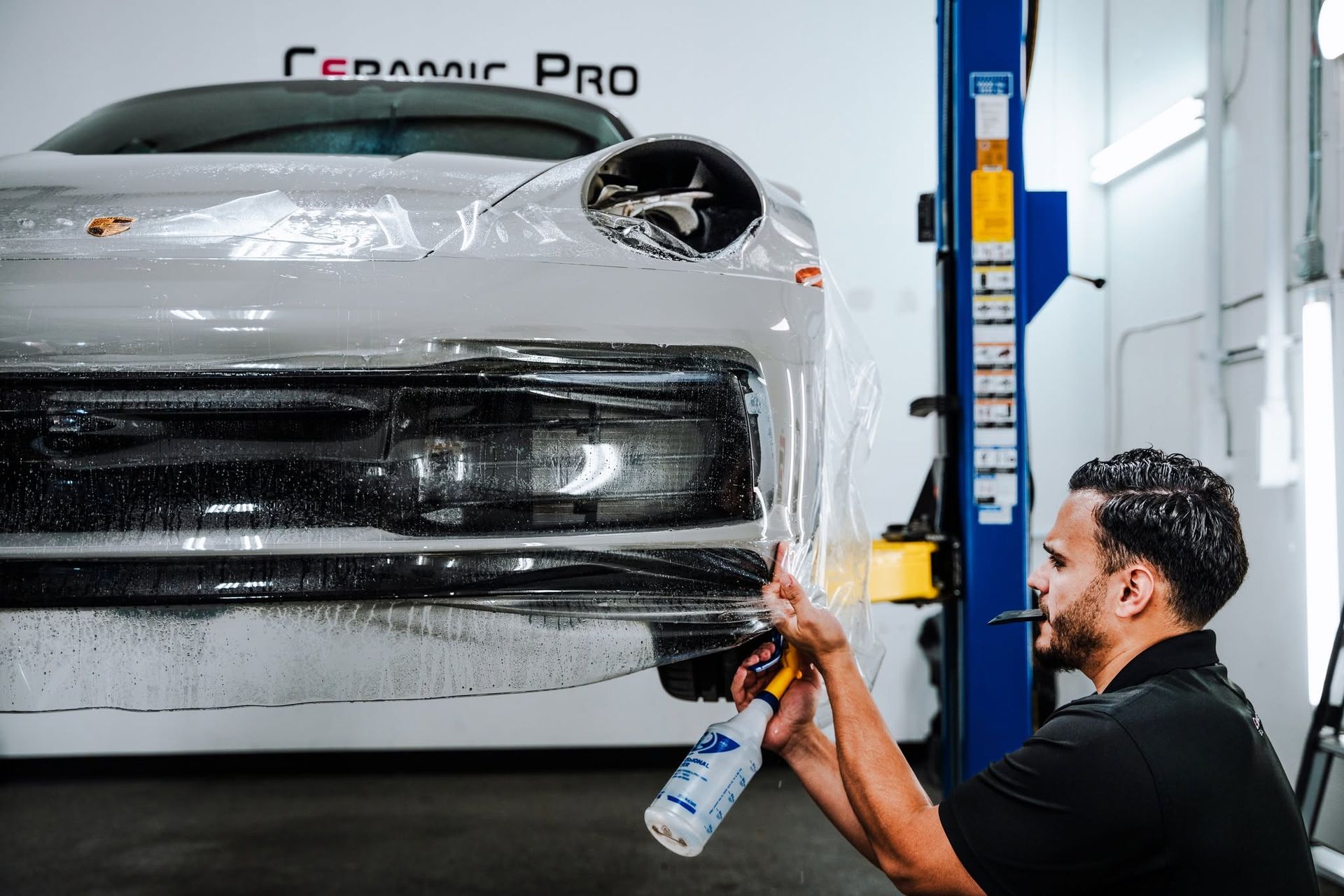 Technician spraying a white car wrap inside an auto detailing shop