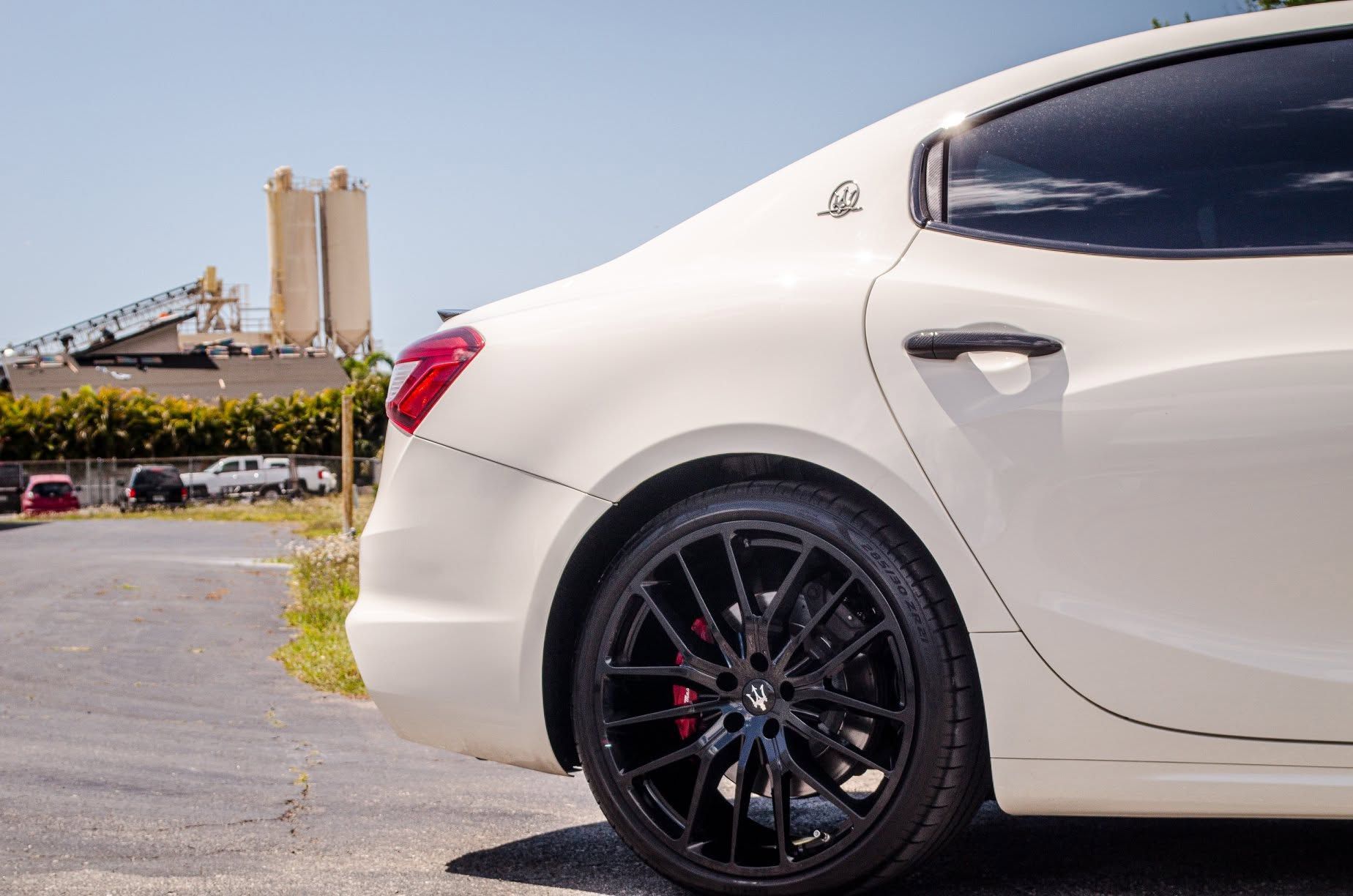 White sports coupe parked near an industrial harbor with a bridge in the background