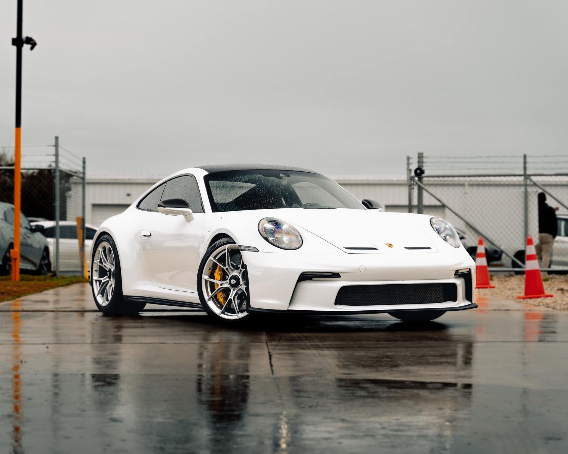 White sports car parked on a wet lot under overcast skies