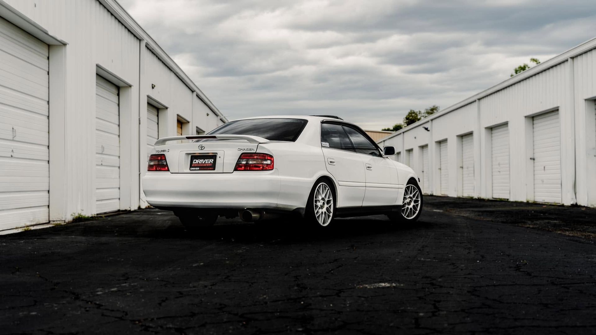White sedan parked in an alley between white garages under a cloudy sky