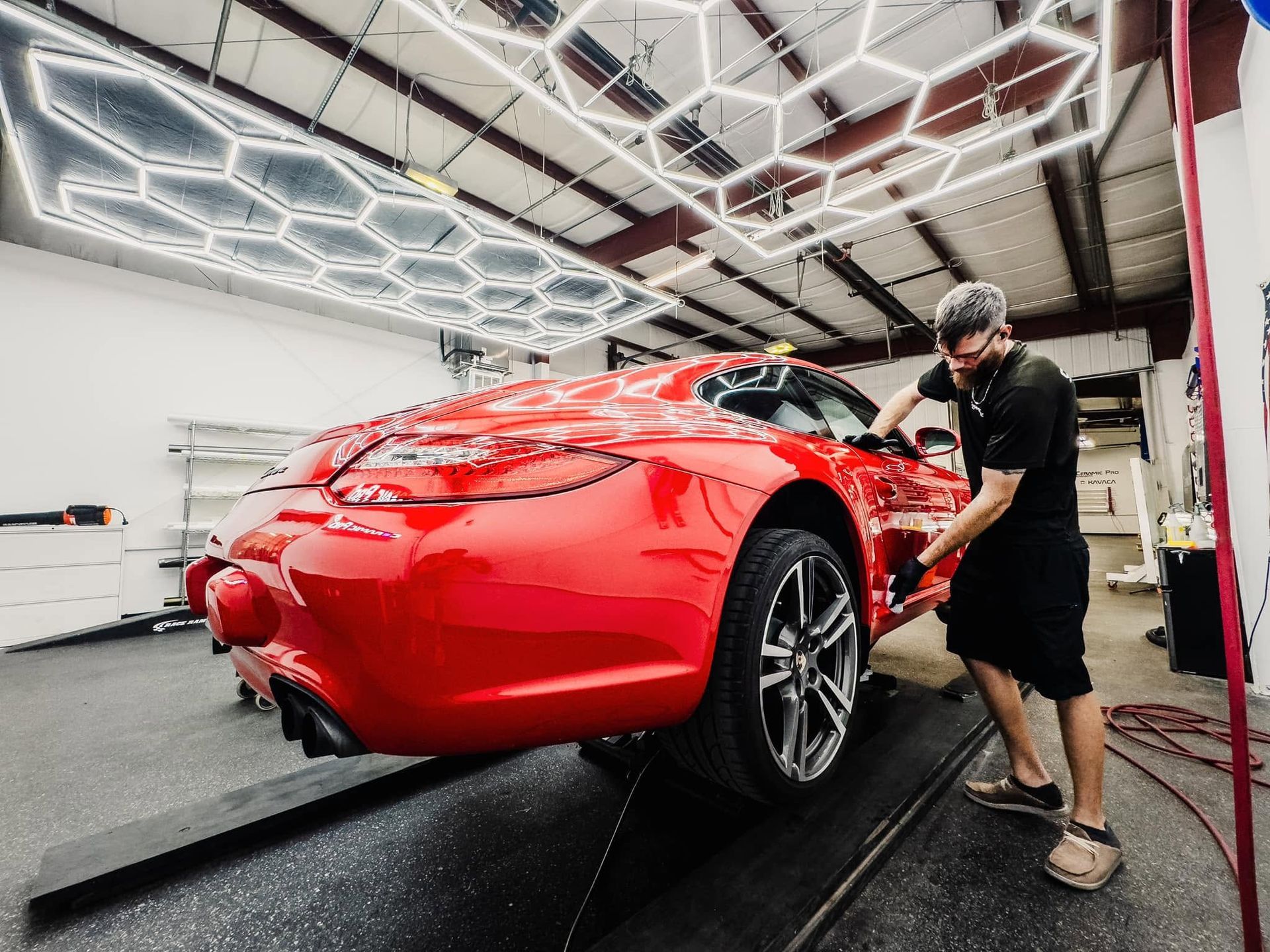 Worker polishing a red sports car in a bright auto detailing shop under geometric ceiling lights