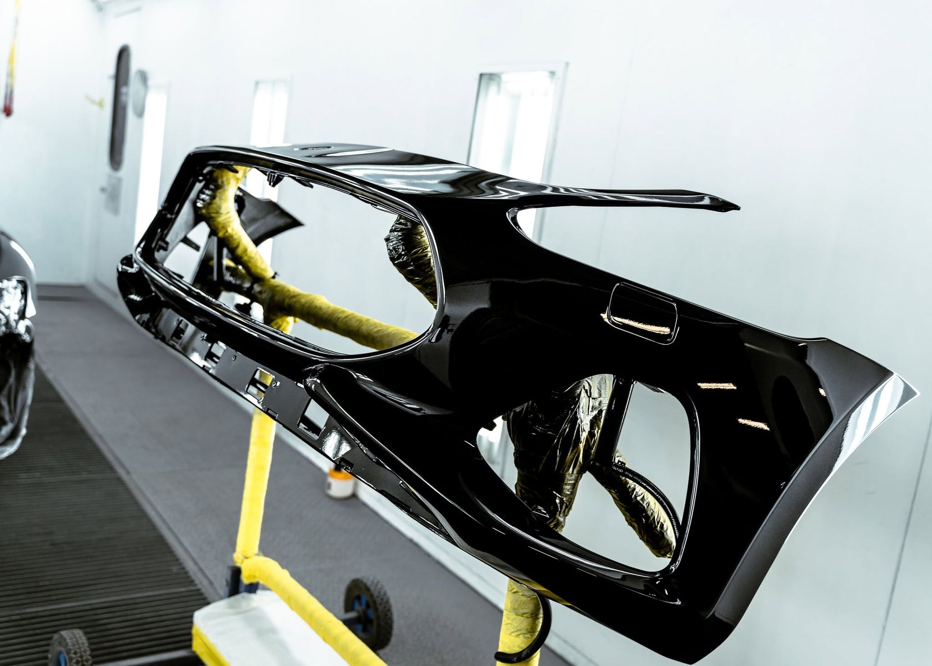 Black car body shell on a stand in a workshop, with yellow supports and a white wall background