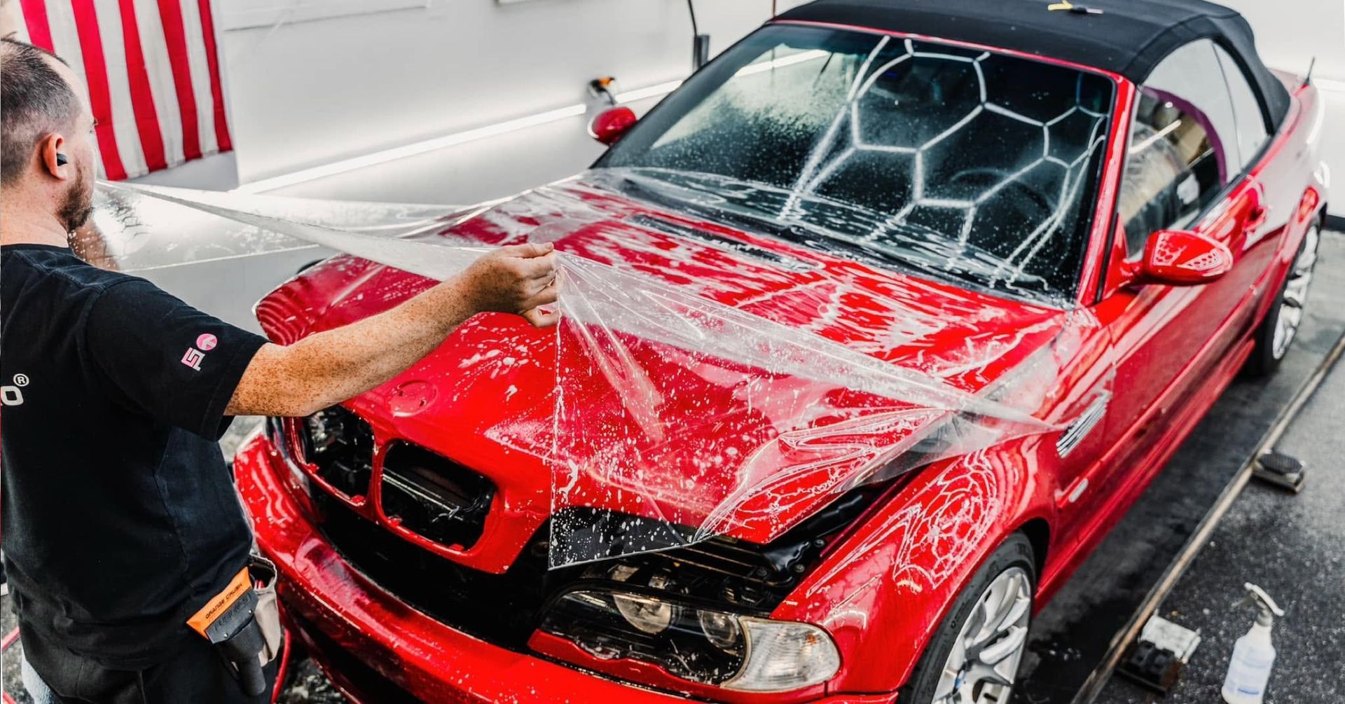 Person washing a red convertible car with soap foam in a car wash garage