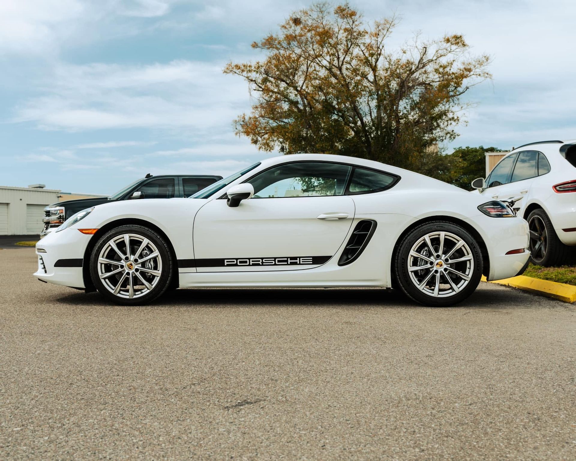 White sports coupe parked outdoors beside a white SUV under a cloudy sky
