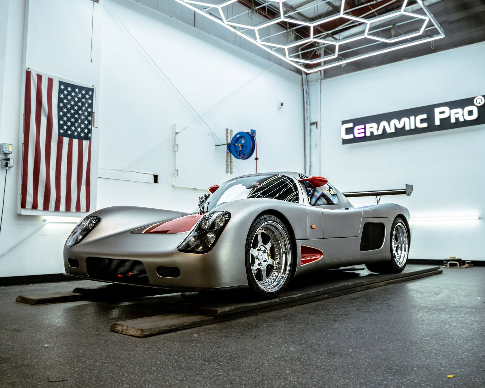 Silver sports car in a glossy garage, with an American flag and Ceramic Pro sign on the walls.