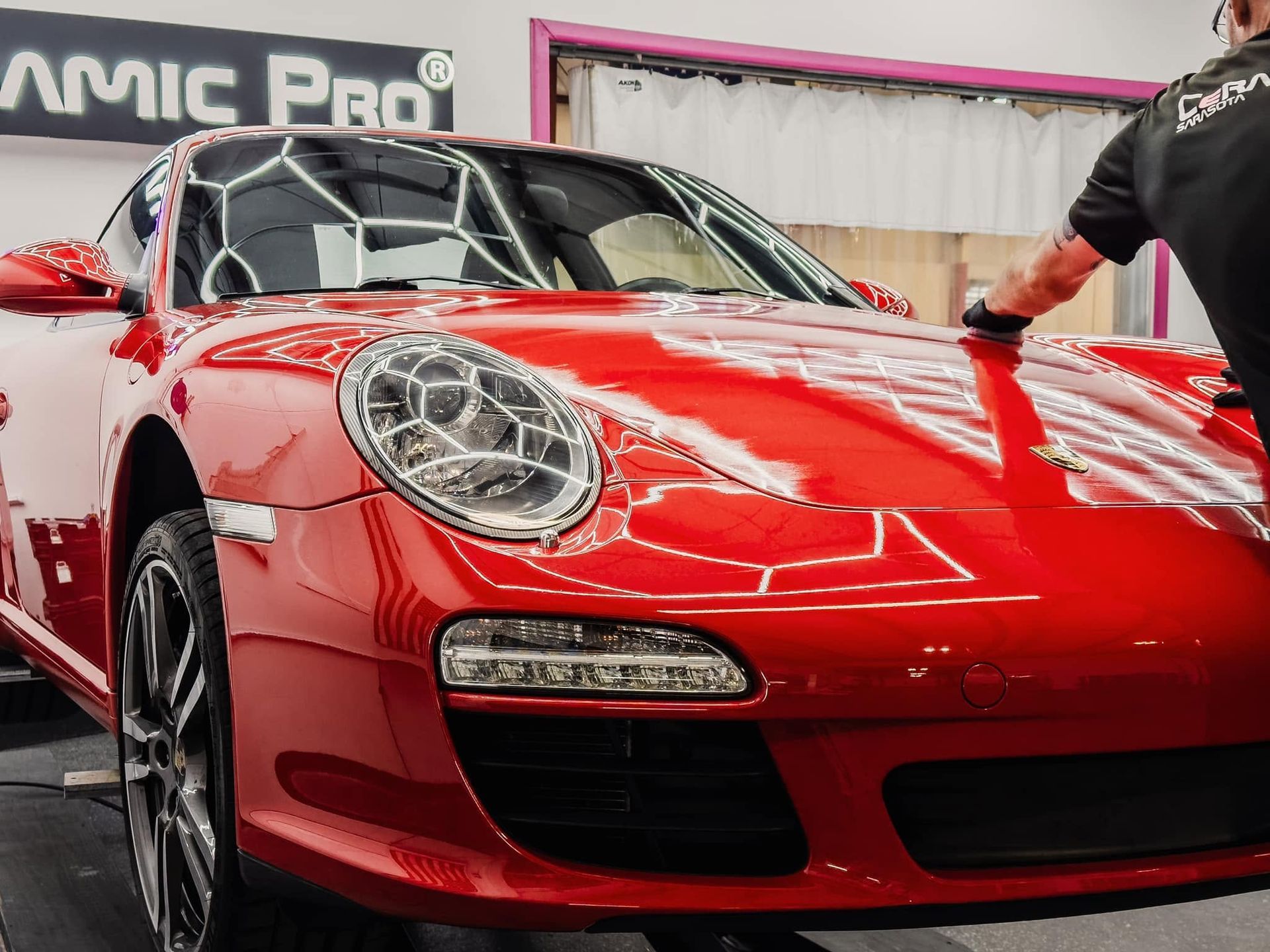 Red sports car in a garage, with a person touching the hood.