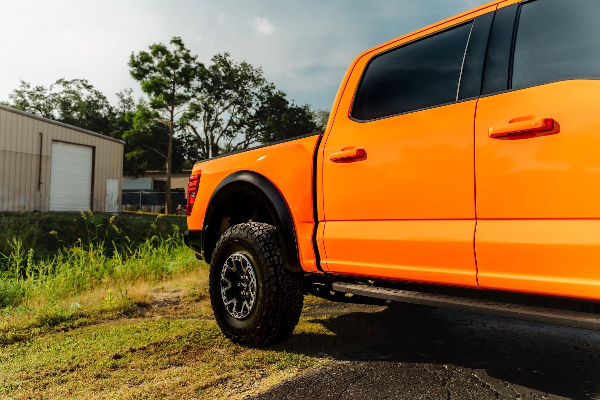 Bright orange pickup truck parked on gravel beside grass near a small building under a cloudy sky