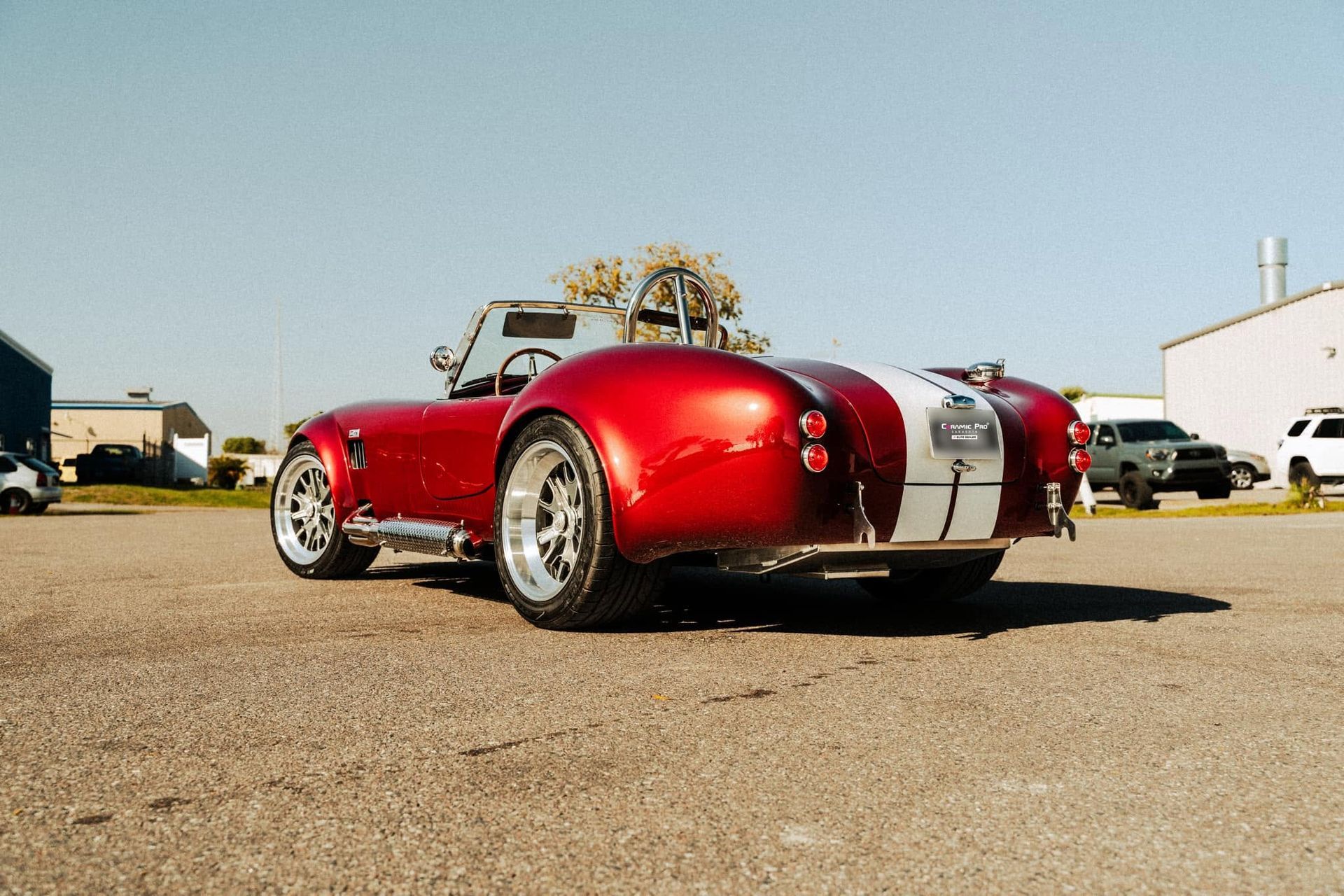 Red vintage sports car with white racing stripes parked on a sunny lot
