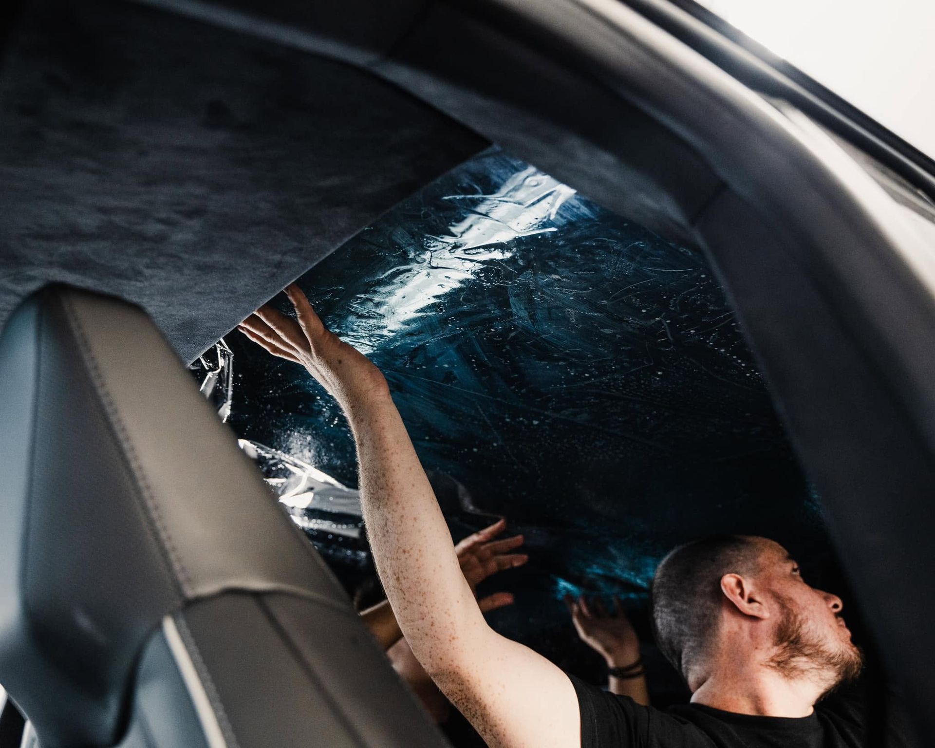 Person in a car reaches up through an open sunroof toward water splashing overhead.