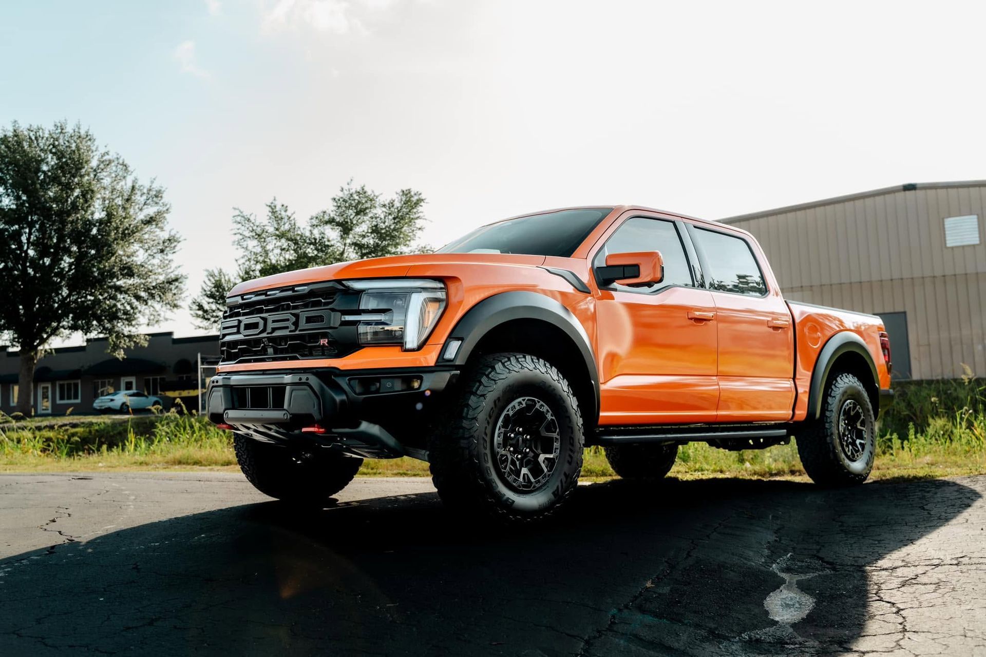 Orange lifted pickup truck parked outdoors on a sunny lot, side view