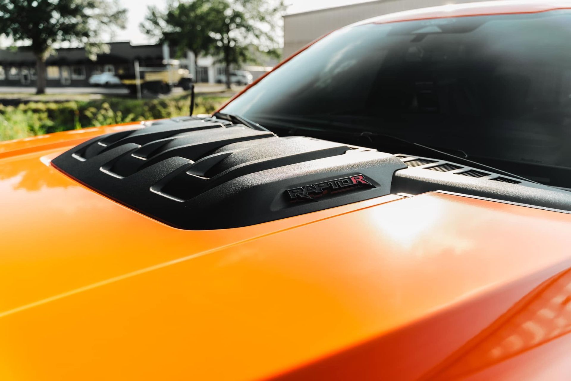 Close-up of an orange sports car hood with black vents in sunlight
