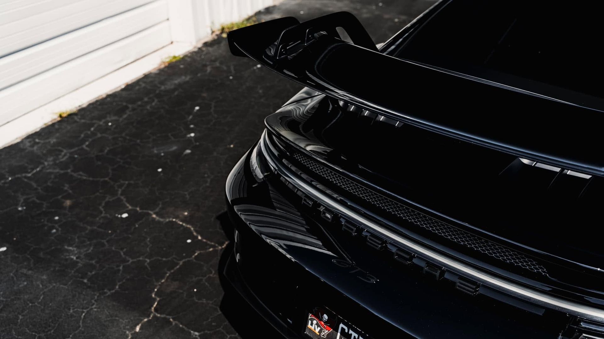 Black sports car parked in a garage, showing the front bumper and glossy hood next to a white wall.