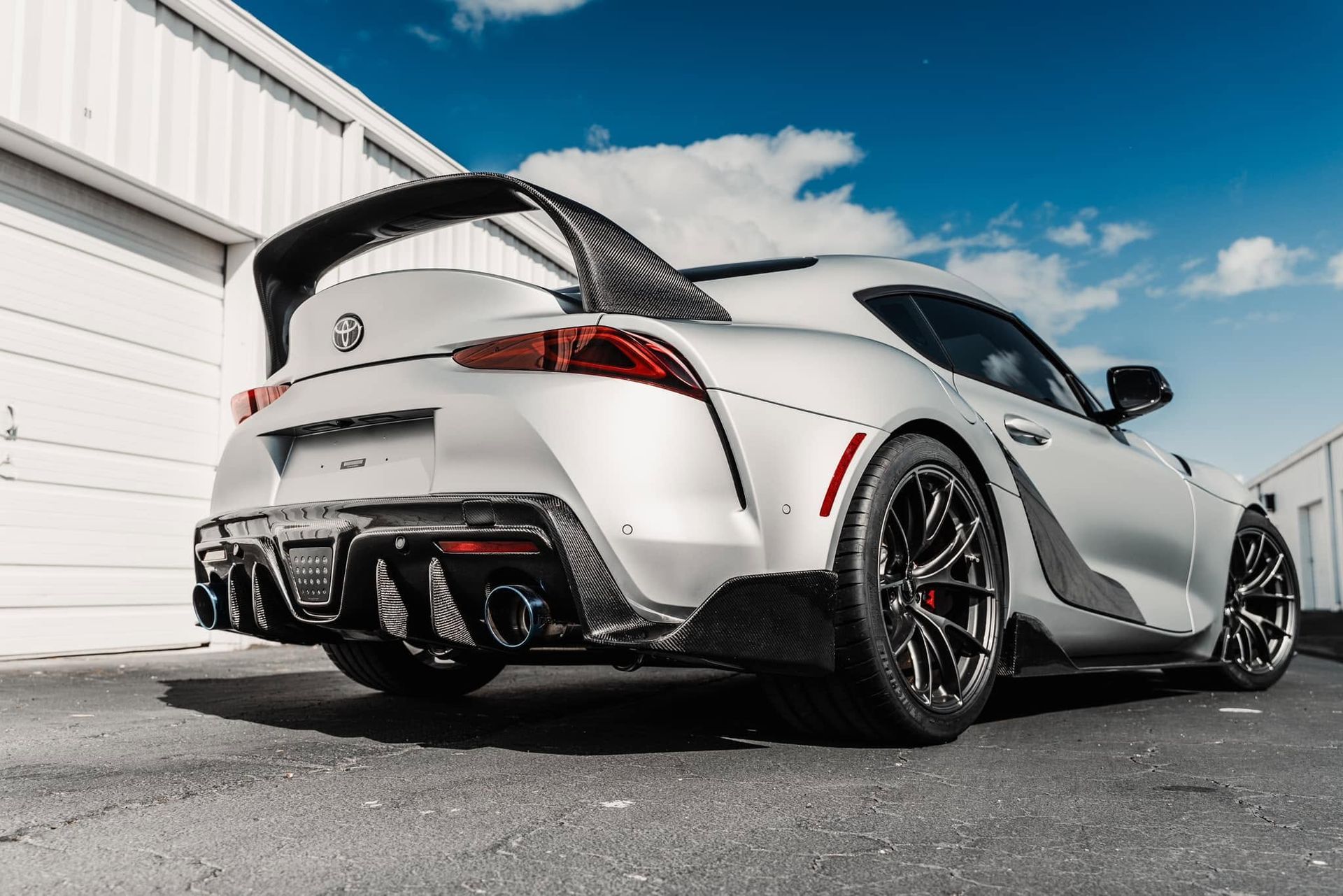 White sports coupe with black accents and large rear spoiler parked beside a building on a sunny day
