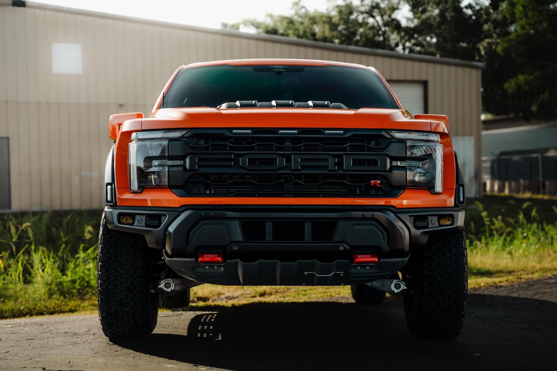 Orange lifted pickup truck front view parked outdoors in front of a metal building