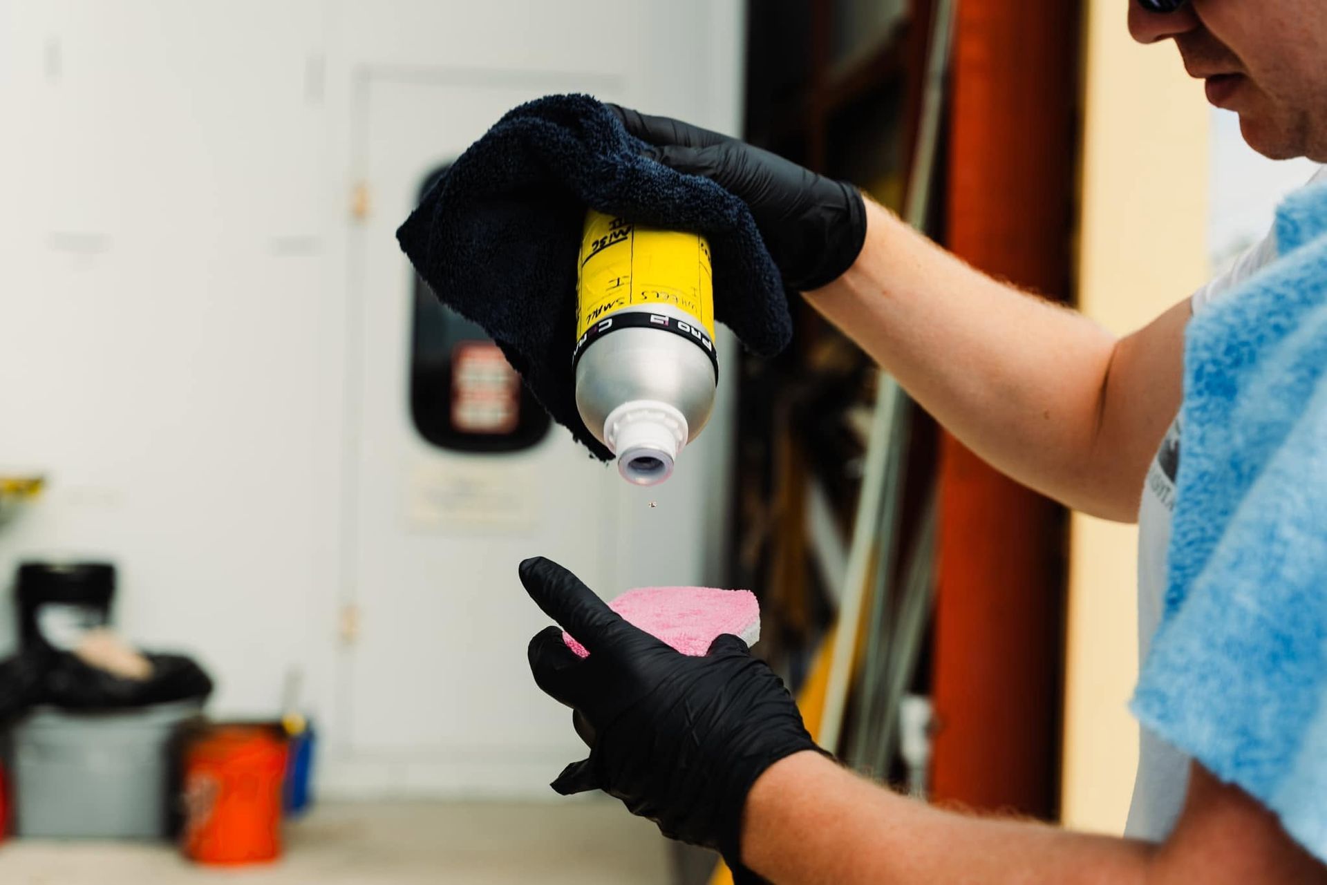 Gloved person applying yellow paint from a spray gun onto a small pink object indoors