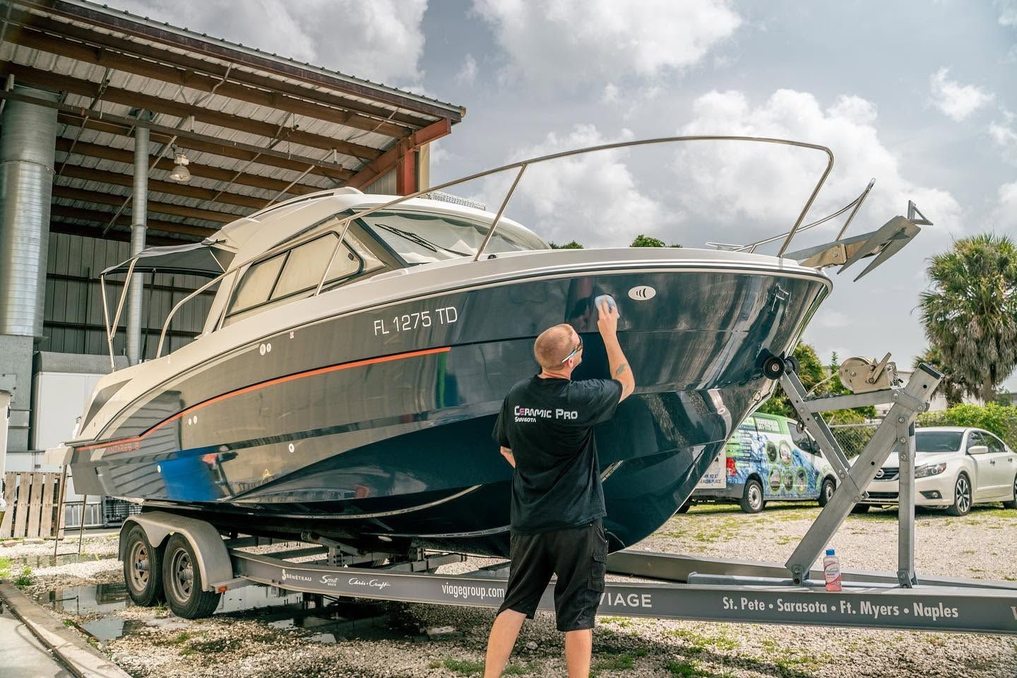 Man standing beside a large white and blue motor yacht on a trailer in a boatyard