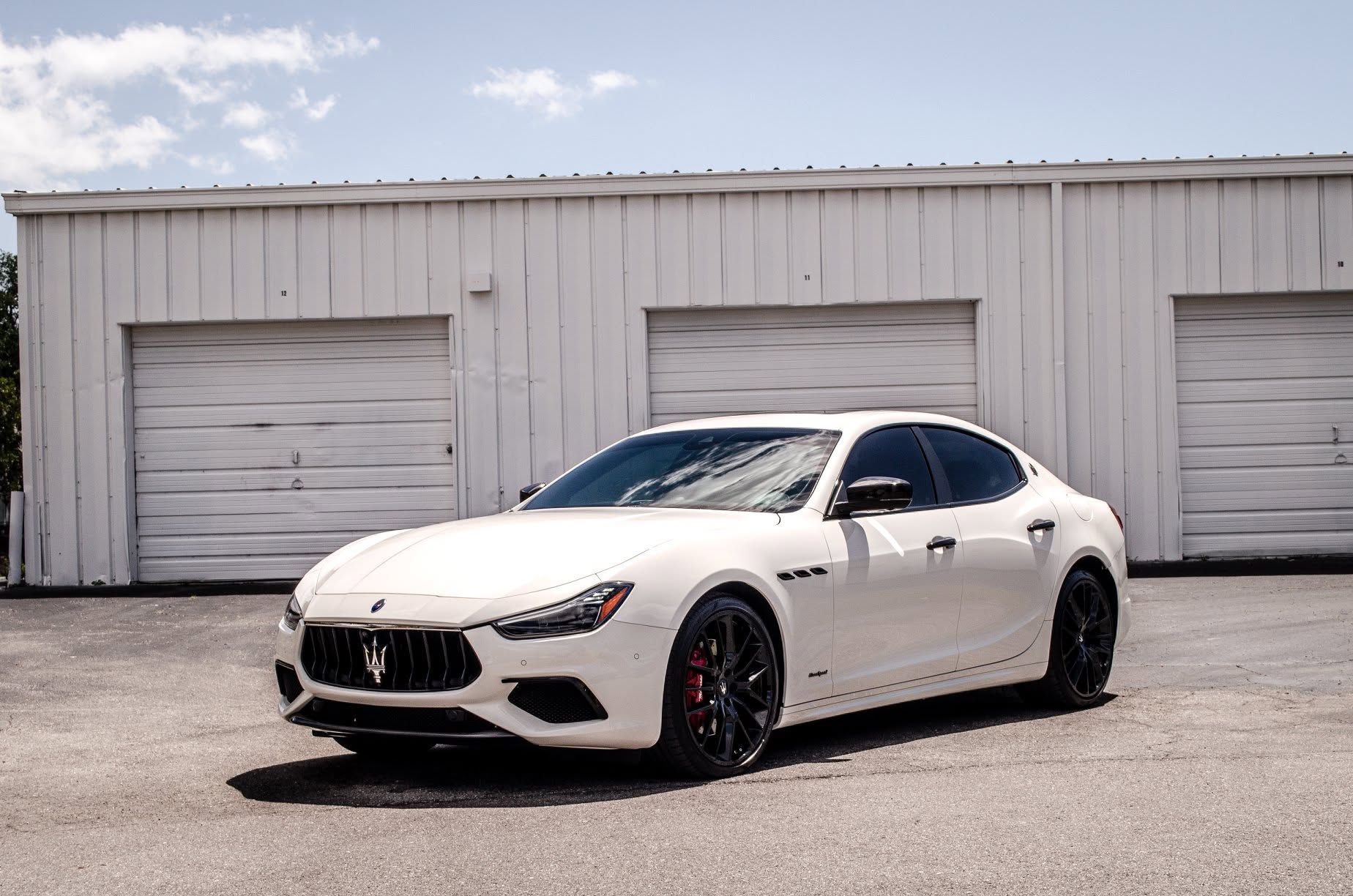 White sports sedan parked in front of a white industrial building with garage doors