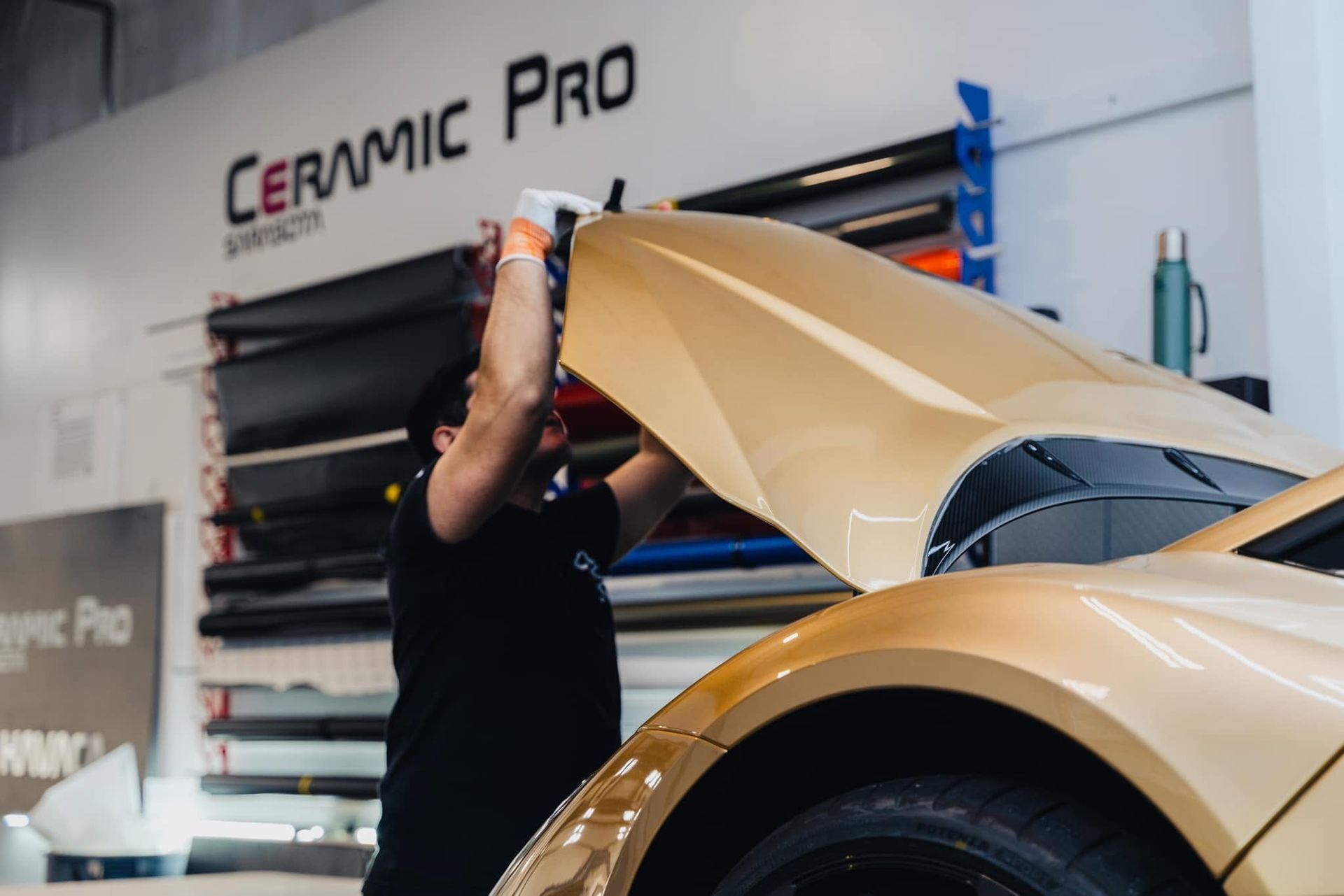 Technician applying ceramic coating to a gold car in an auto detailing shop