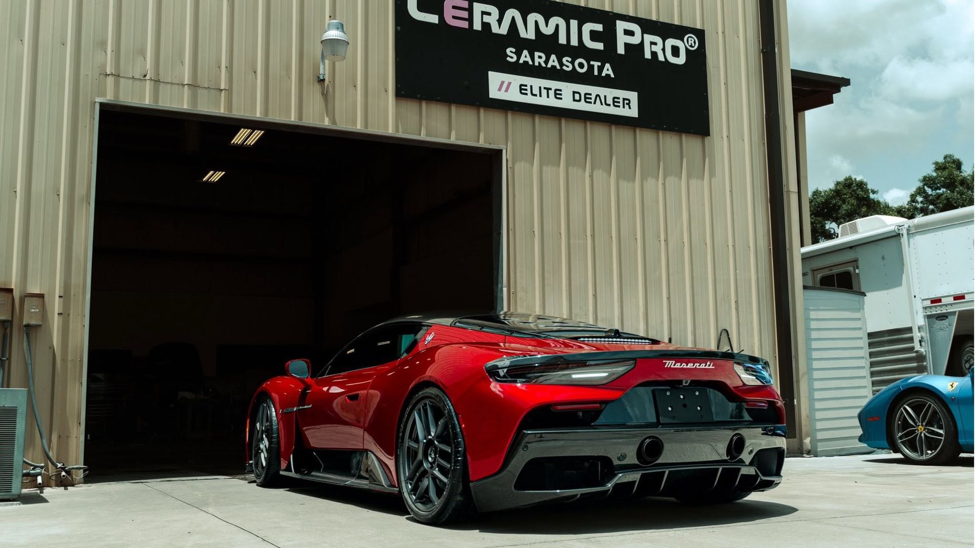 Red sports car parked in a garage entrance beside a Ceramic Pro sign