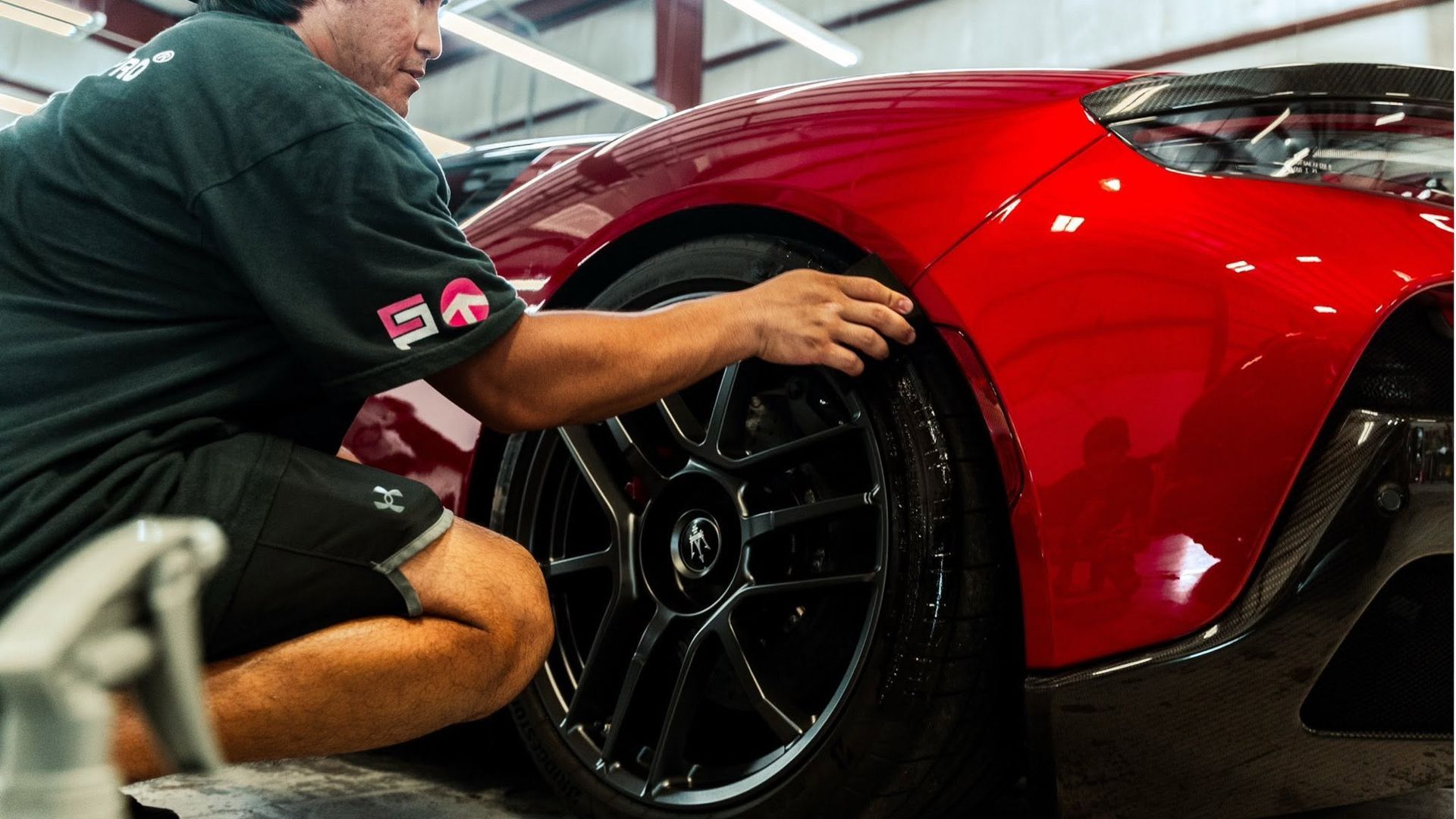 Mechanic kneeling beside a red sports car, adjusting the front wheel in a garage.