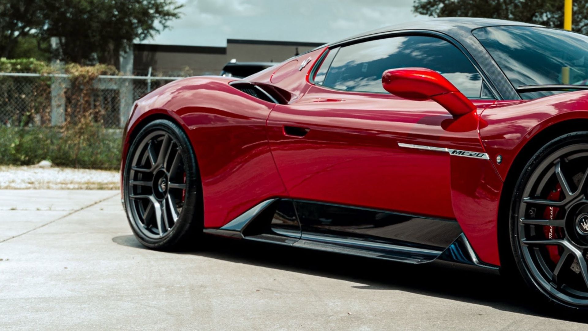 Red sports car parked on a driveway, side view with black wheels and red accents.