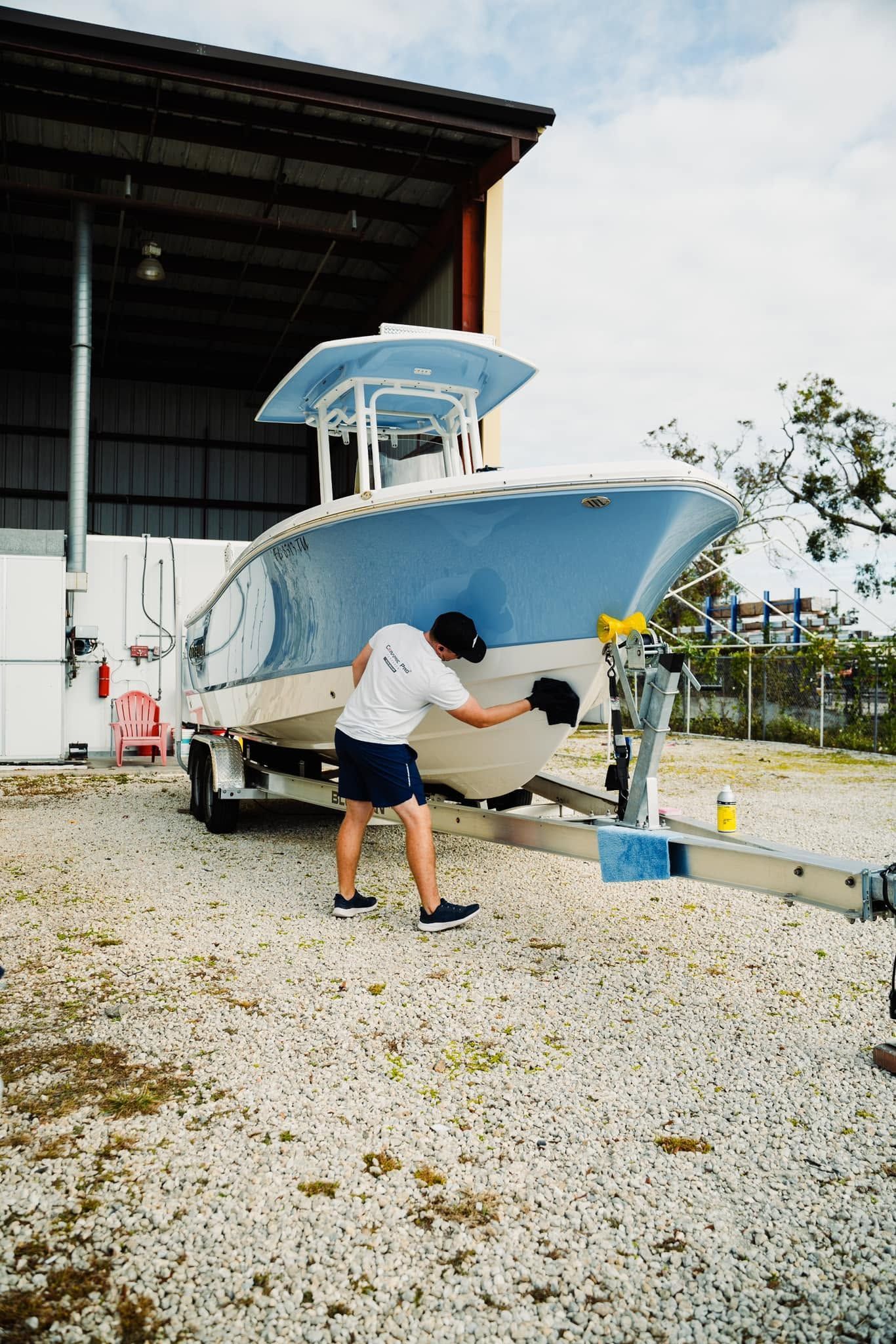 Person cleaning the hull of a blue boat on gravel beside a dockside building