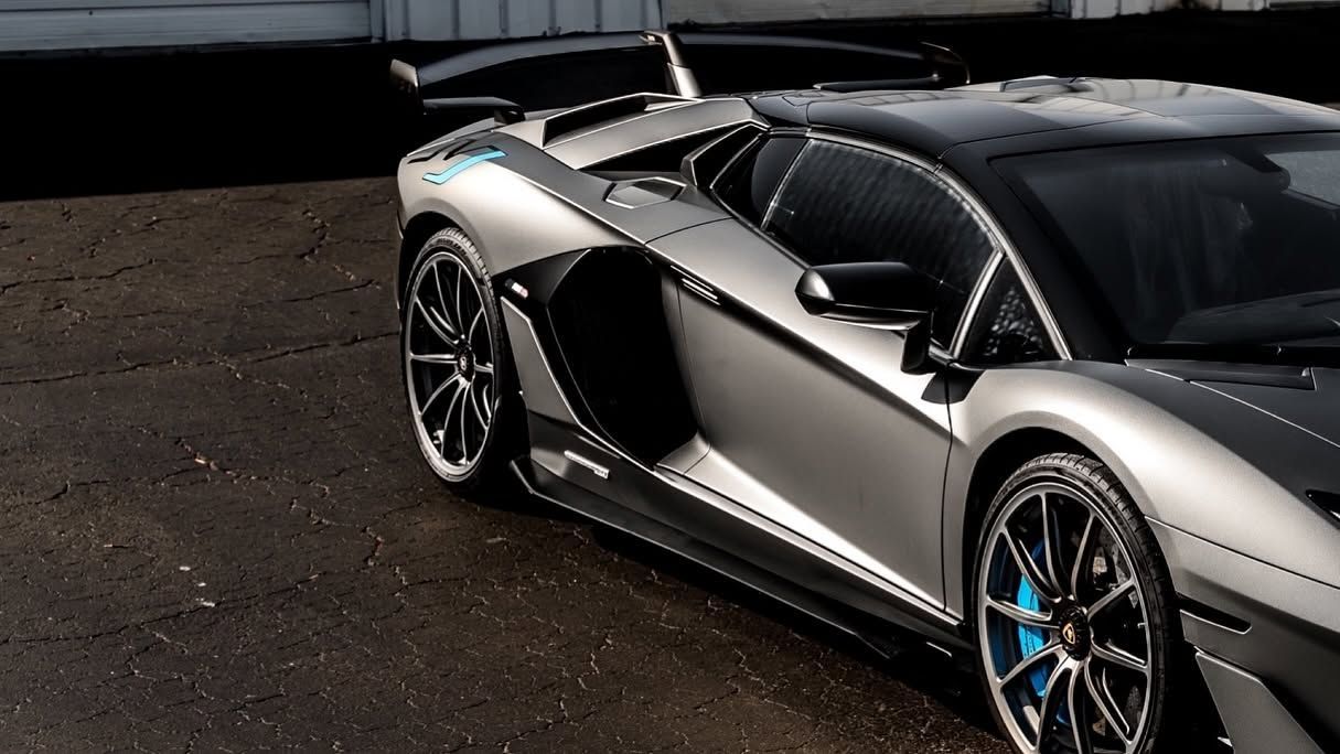 Silver sports car parked on dark pavement, viewed from the side with blue-accented rims.