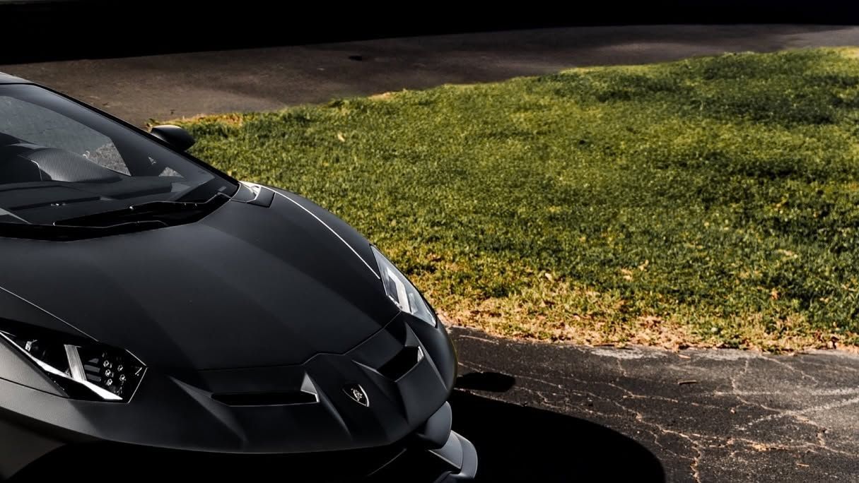 Black sports car parked beside a grassy lawn along a paved driveway.