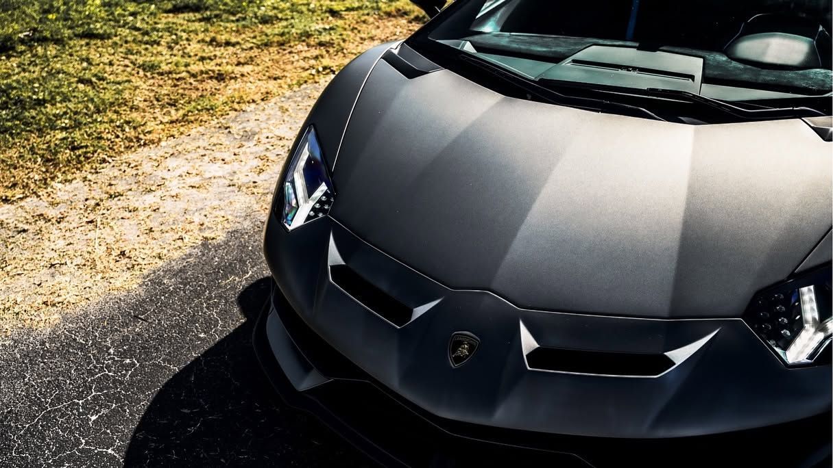Front view of a matte black sports car parked beside a gravel path in sunlight