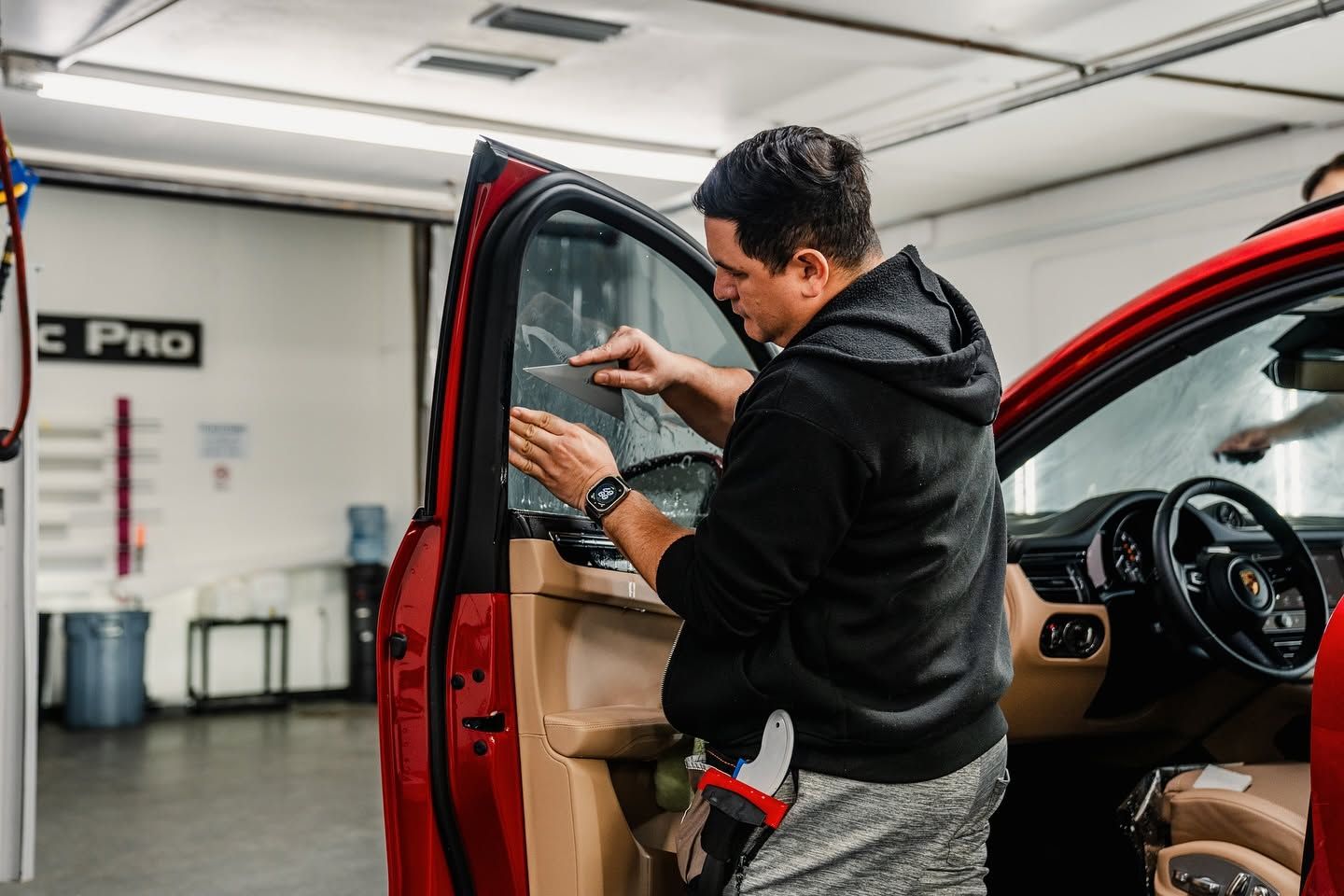 Man adjusting the open door of a red car inside an auto shop
