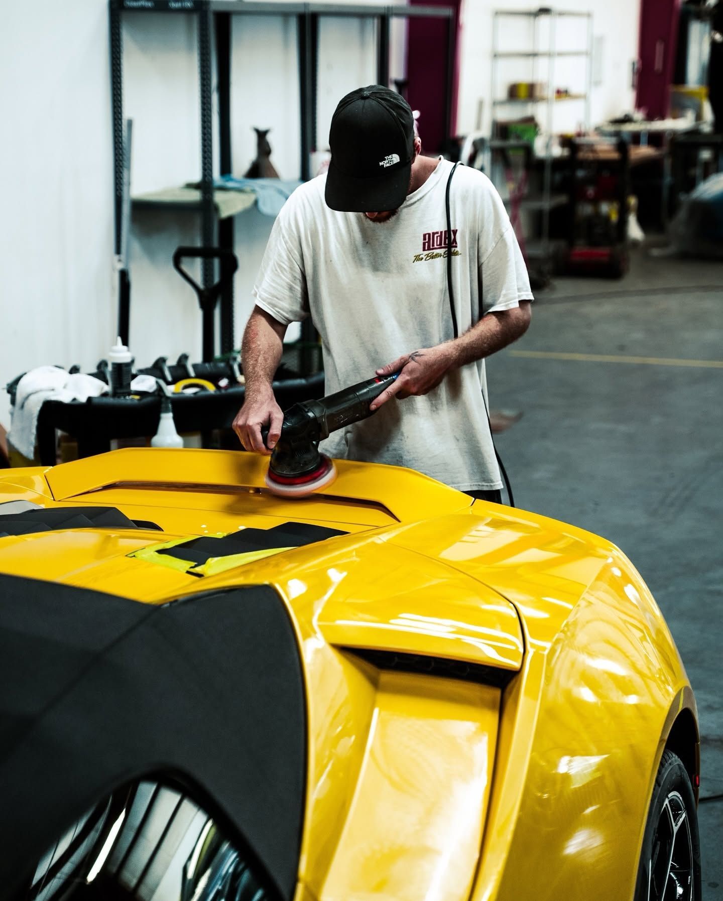 Person polishing a yellow sports car in a garage workshop