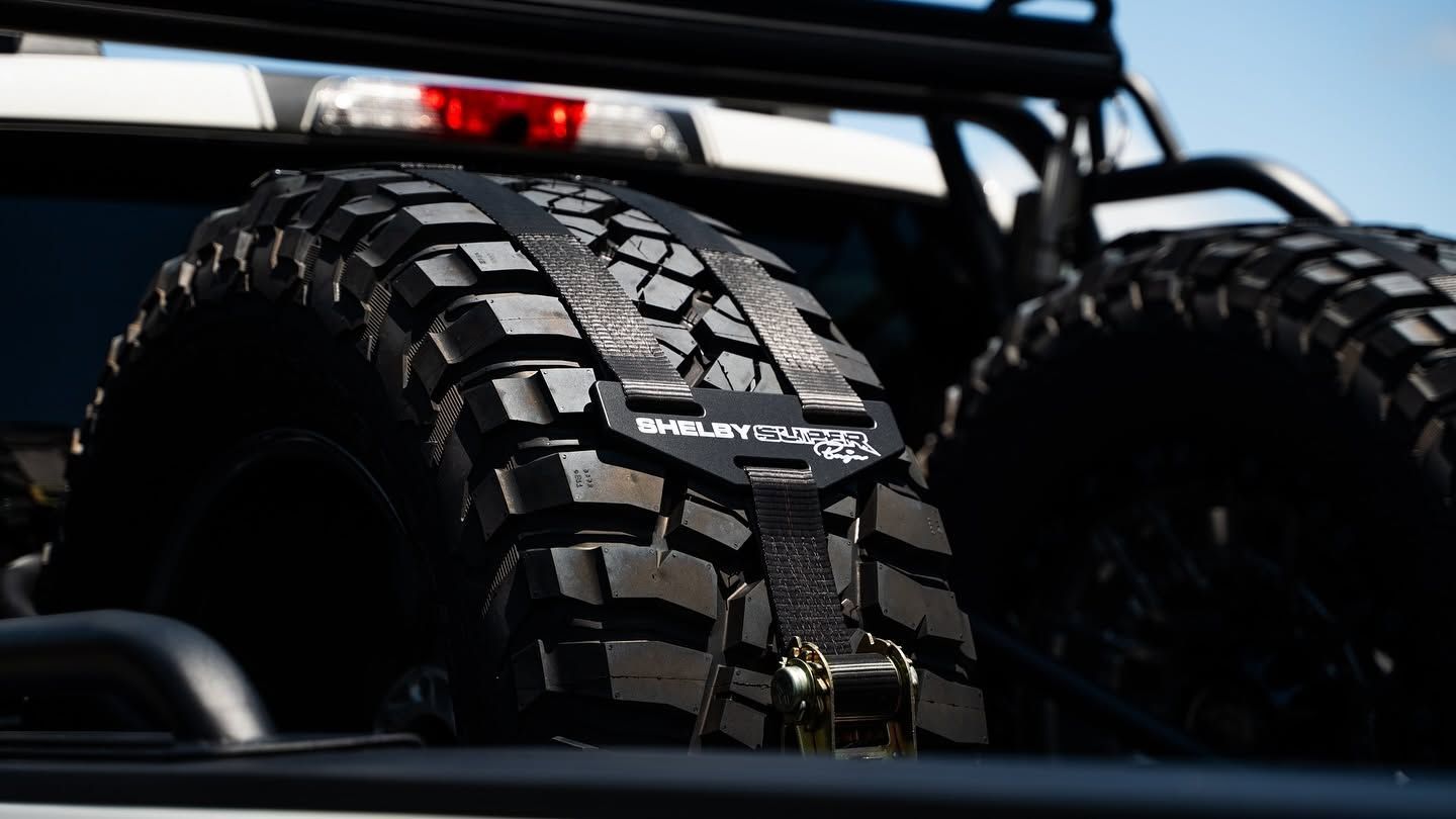 Close-up of rugged off-road tires on a vehicle, viewed from the rear with a roof rack above.