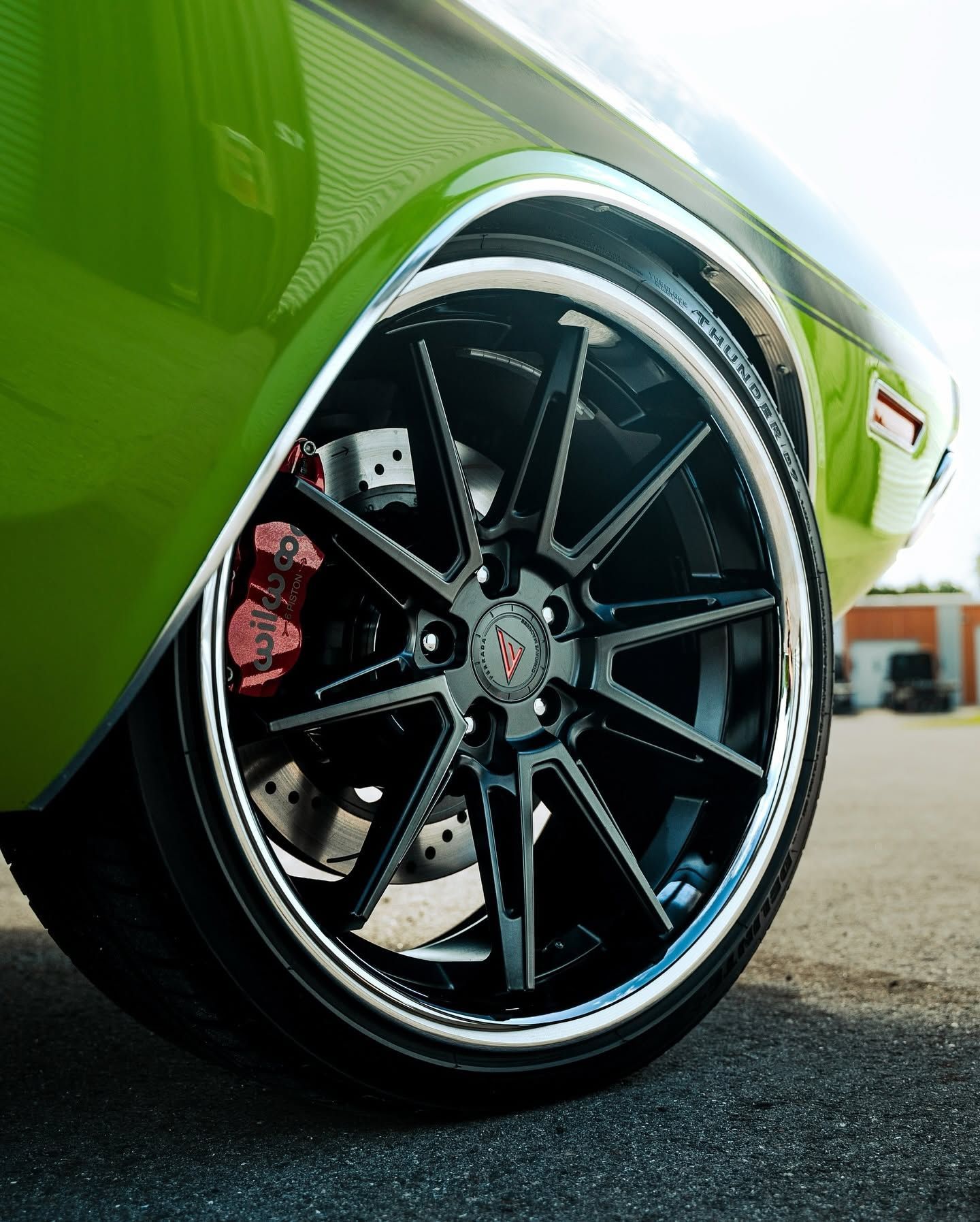 Close-up of a green sports car’s black alloy wheel with red brake caliper on pavement