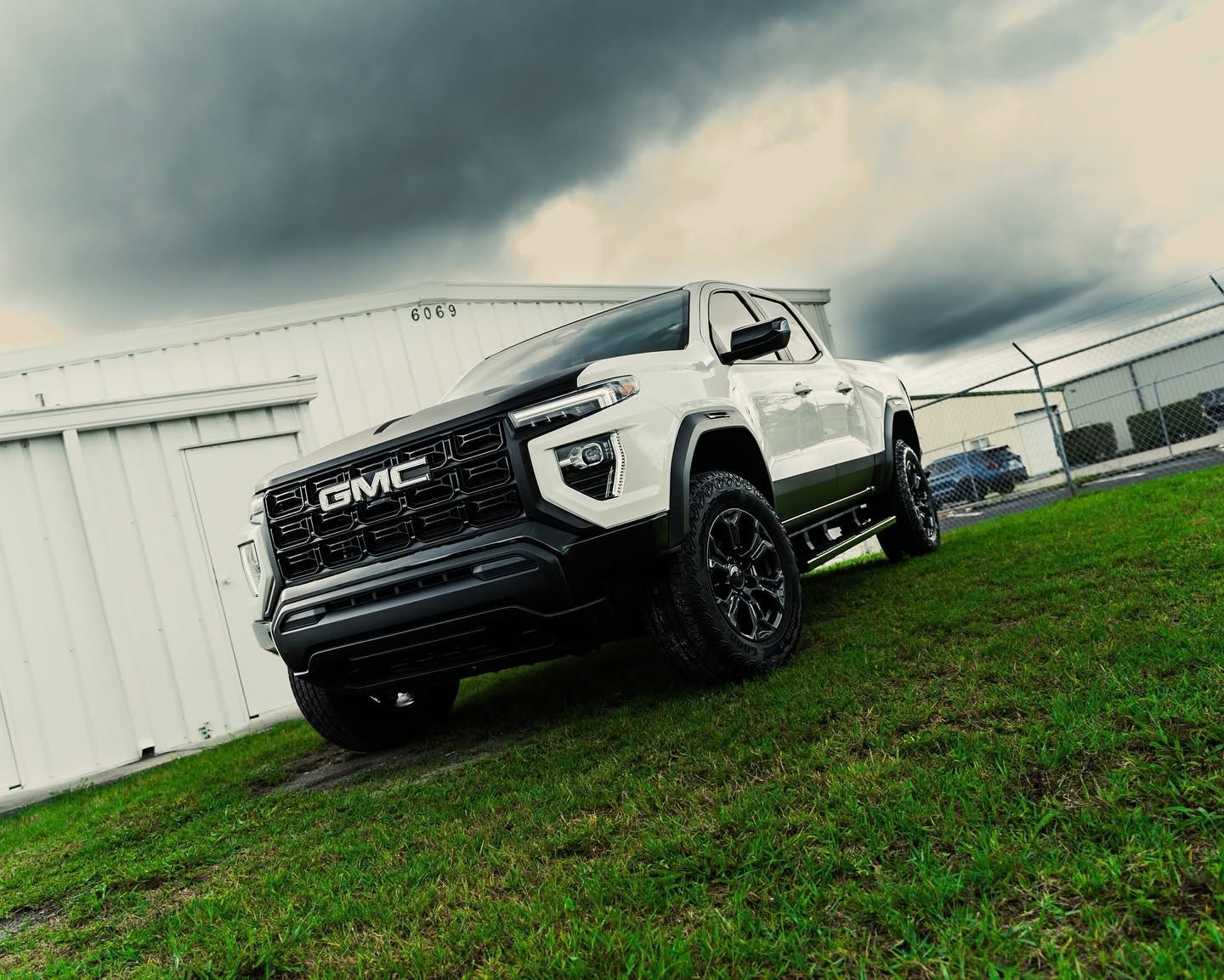 White GMC pickup truck parked on grass beside a building under a cloudy sky