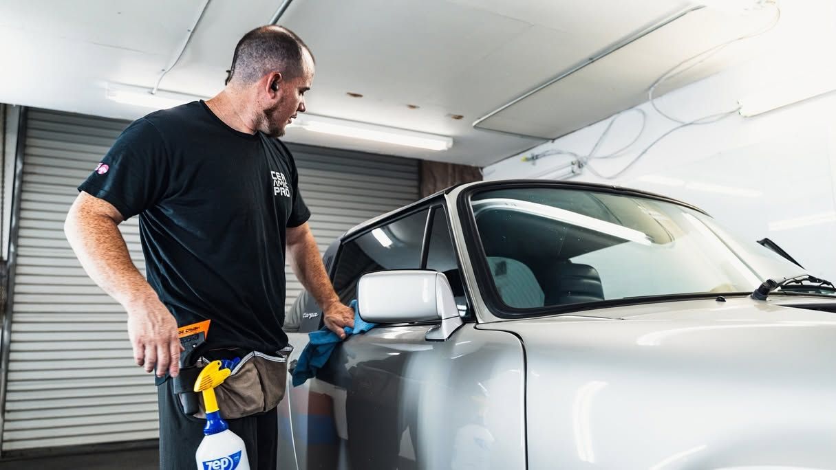 Man cleaning a silver car in a garage with a spray bottle