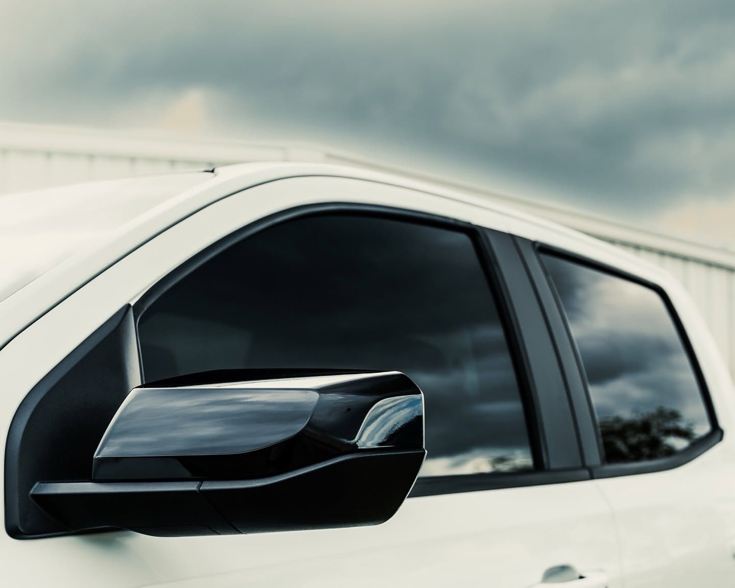 Black side mirror on a white car against a cloudy sky