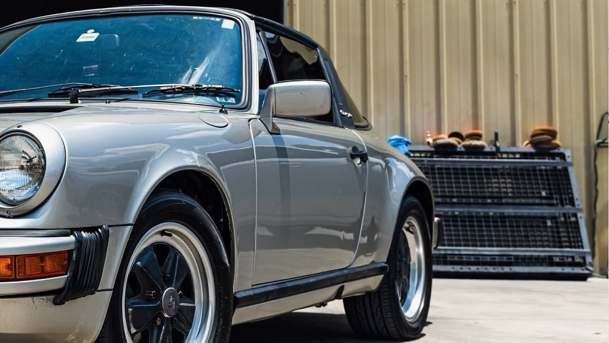 Silver classic car parked beside stacked black crates outdoors.