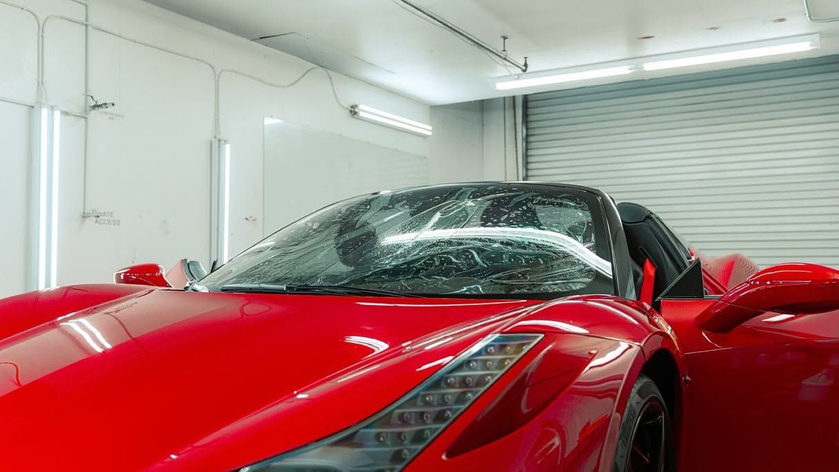 Red sports car covered in snow inside a bright garage with the door open.