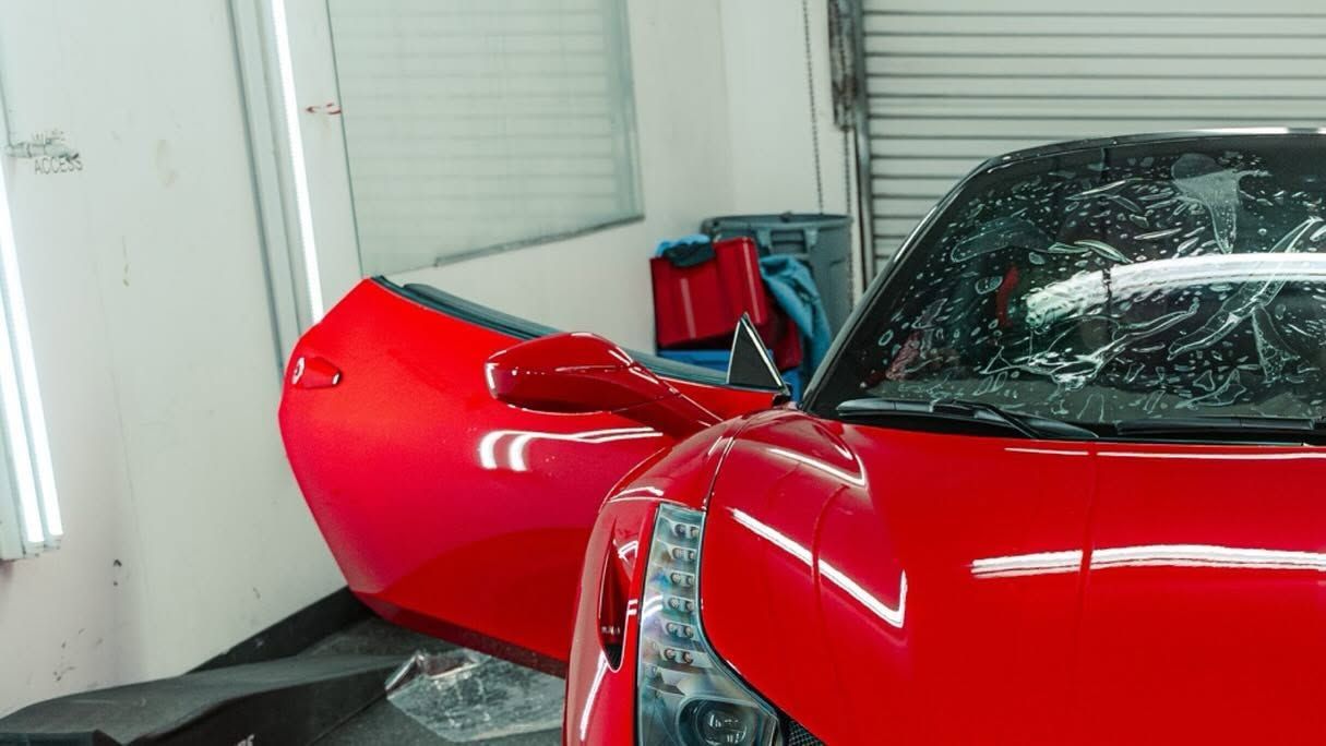 Red sports car with a damaged front end and detached door in a garage or repair bay