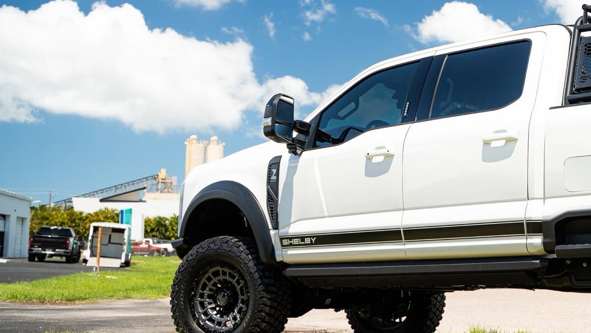 White lifted pickup truck parked in a sunny suburban driveway near a house