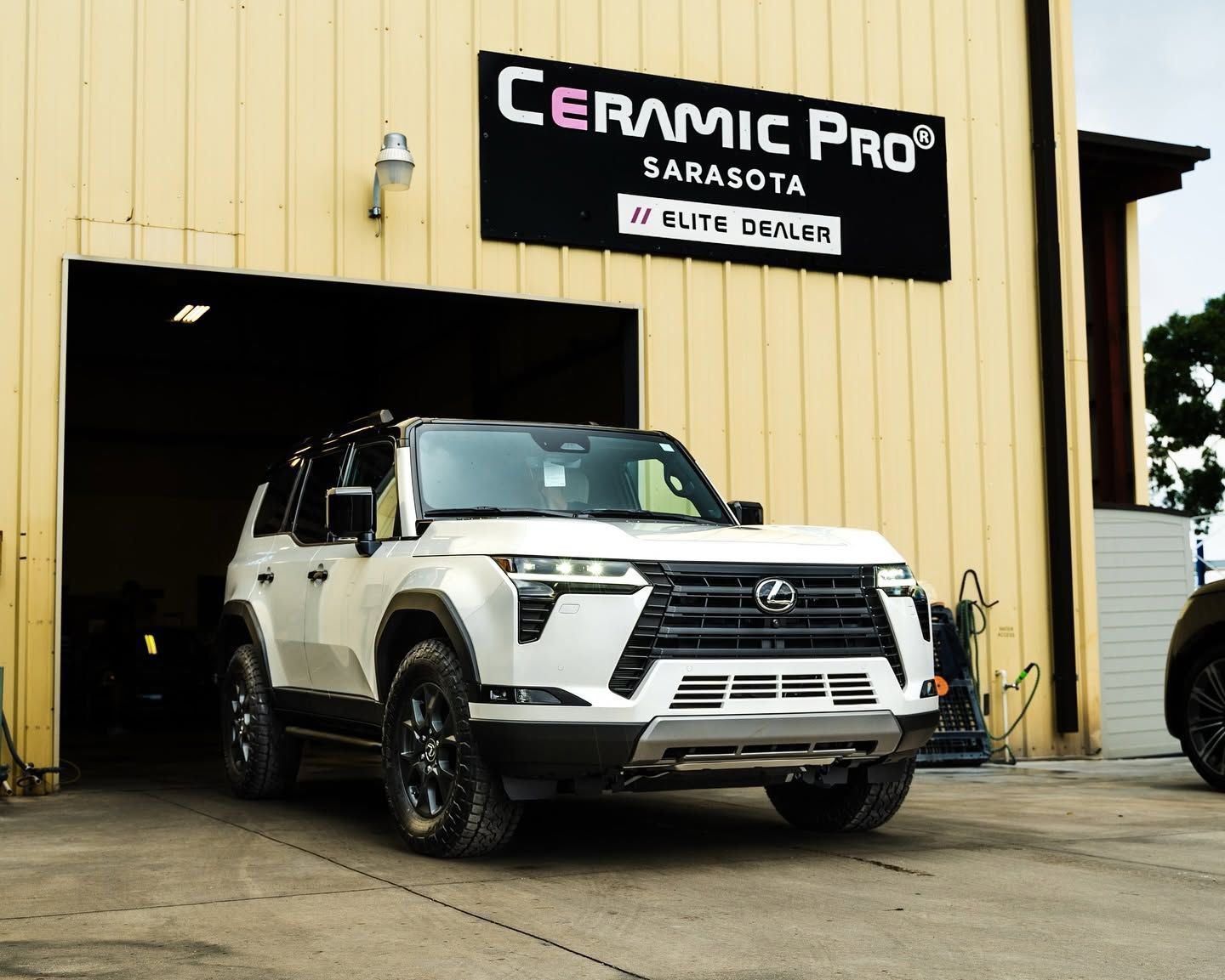 White SUV parked outside Ceramic Pro Sarasota auto detailing shop under a beige awning.