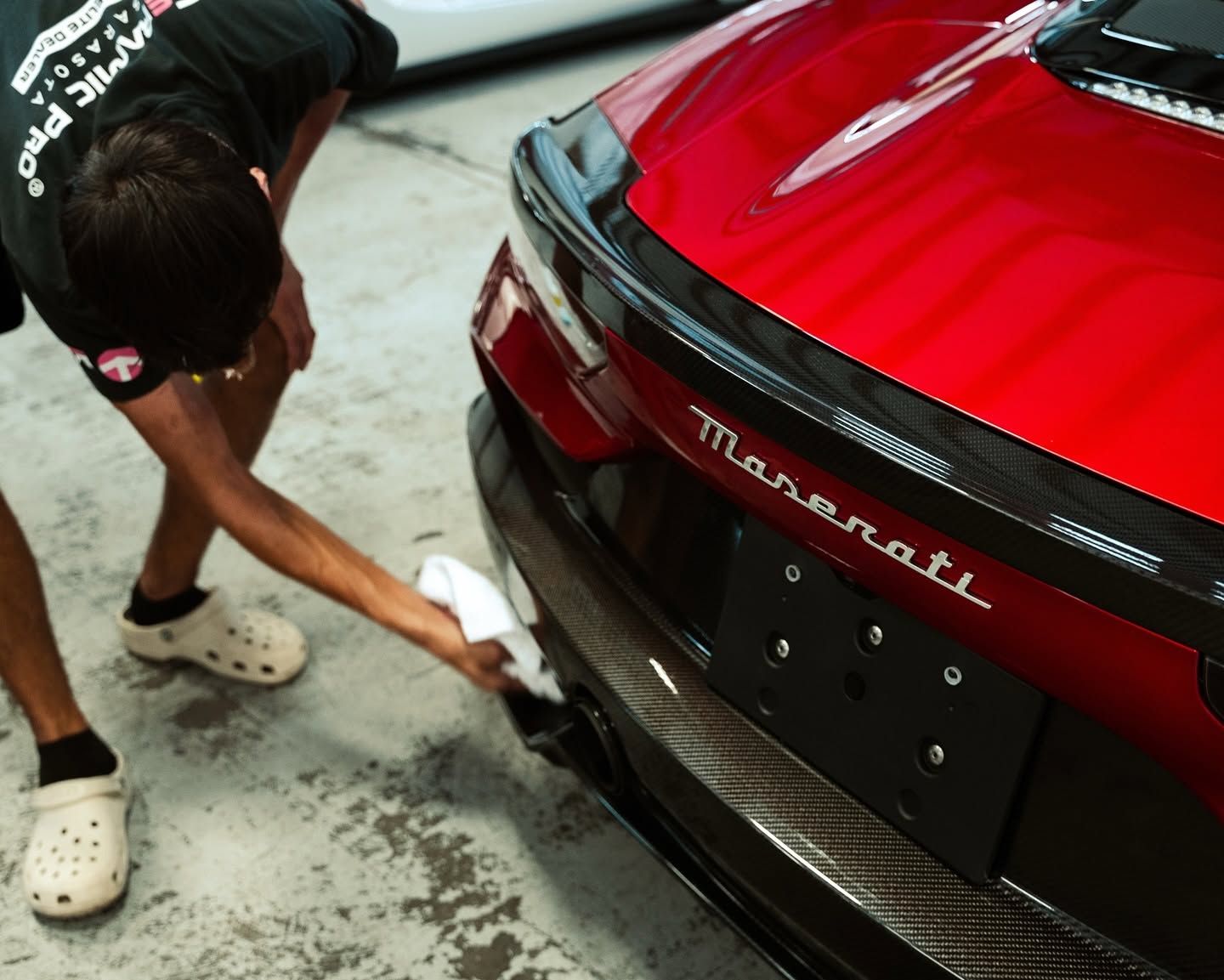 Person cleaning the rear of a red Maserati sports car in a garage