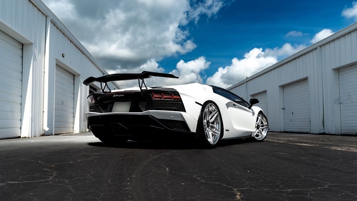 White sports car in an industrial alley, low rear angle with cloudy blue sky above
