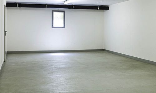 An empty basement with white walls and a window.