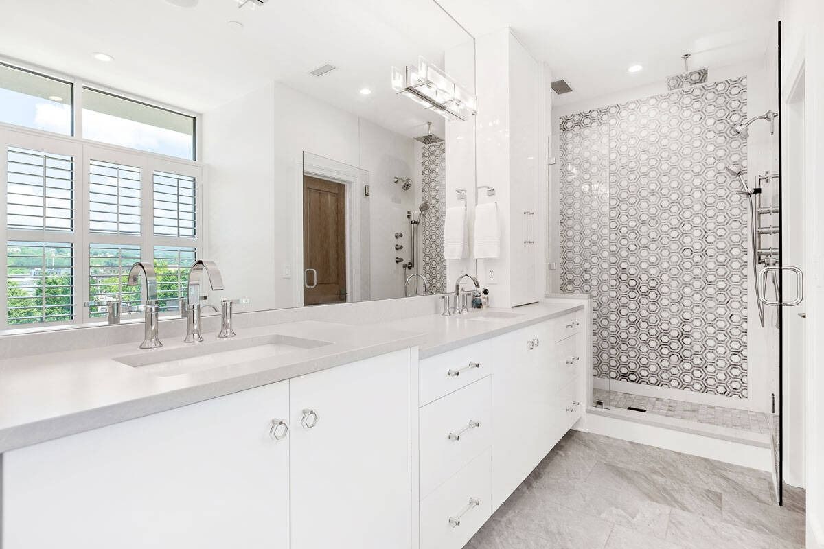 Bright white bathroom with double vanity, large mirror, and tiled walk-in shower