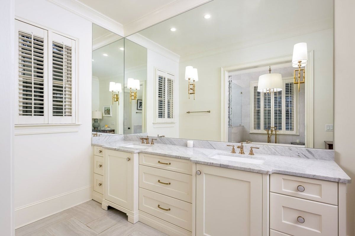 Bright white bathroom vanity with marble countertop, large mirror, and plantation shutters