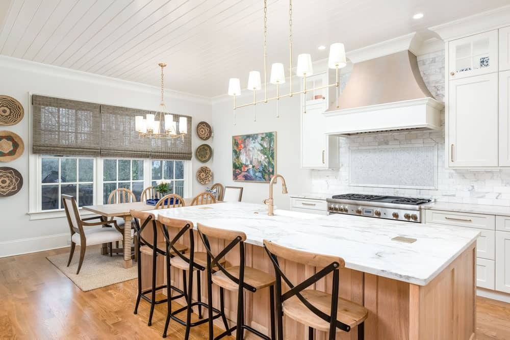 Bright modern kitchen with marble island, pendant lights, bar stools, and large windows